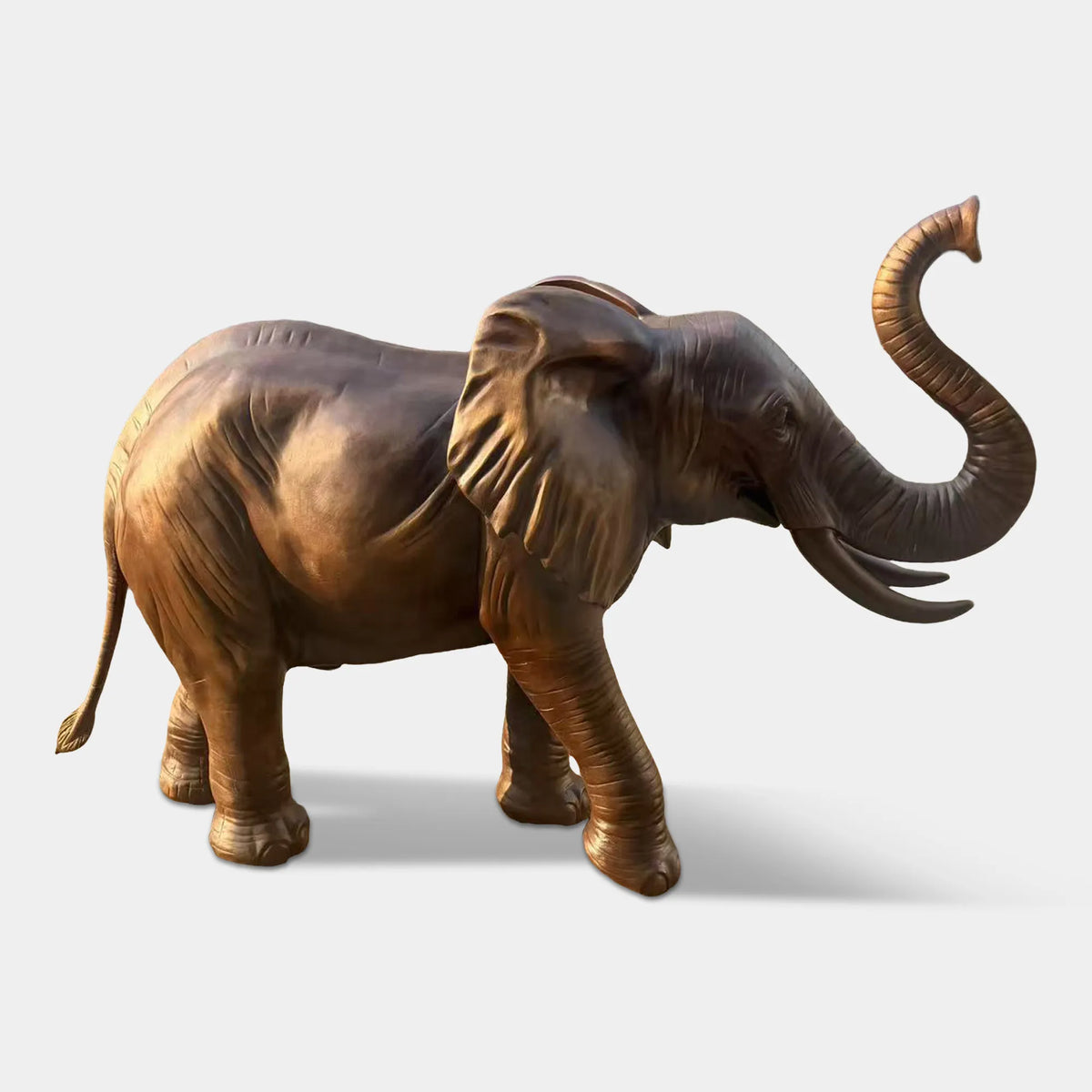 A bronze elephant statue with raised trunk stands along a shaded park walking path.