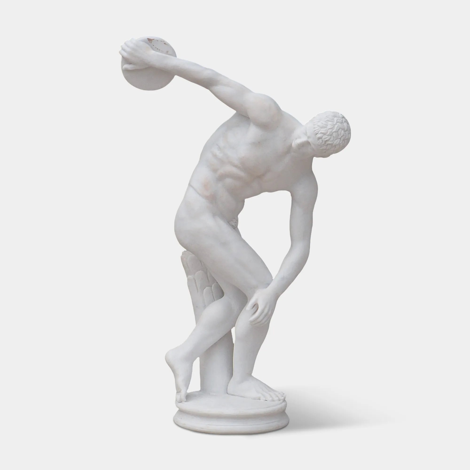 White marble discus thrower statue in dynamic pose in a classical Greek style garden with stone columns and greenery.
