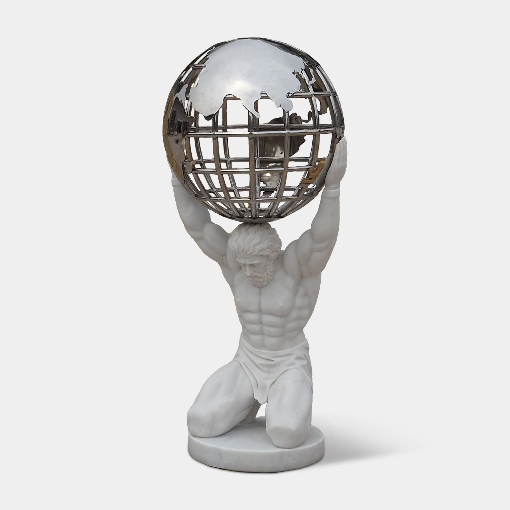 Decorative marble Atlas statue kneeling and holding a stainless steel sphere above his shoulders in front of a floor-to-ceiling window indoors.