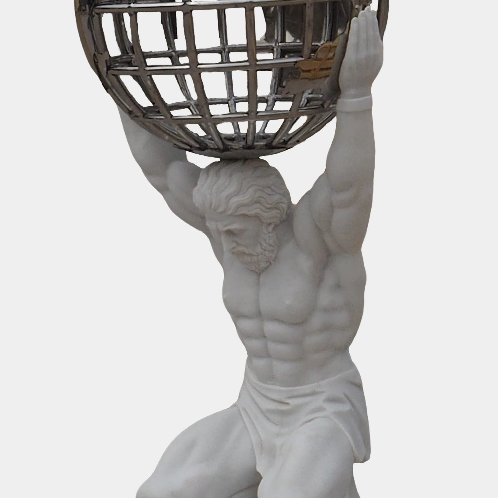 Decorative marble Atlas statue kneeling and holding a stainless steel sphere above his shoulders in front of a floor-to-ceiling window indoors.