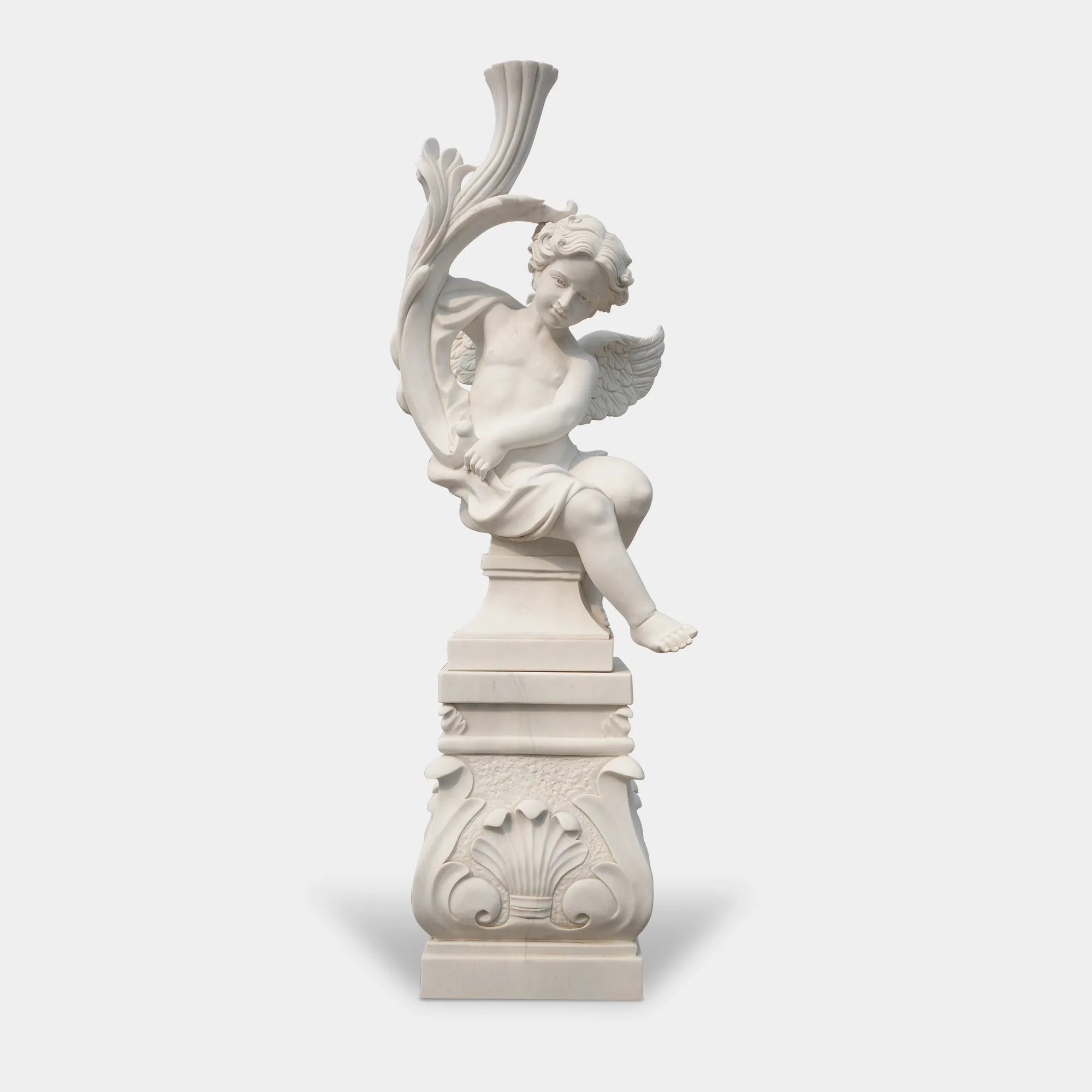 Cute cherub angel statue in white marble with wings sitting pose on base in a garden