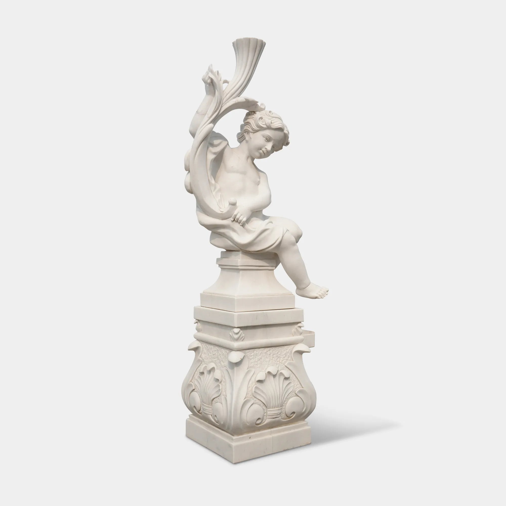 Cute cherub angel statue in white marble with wings sitting pose on base in a garden