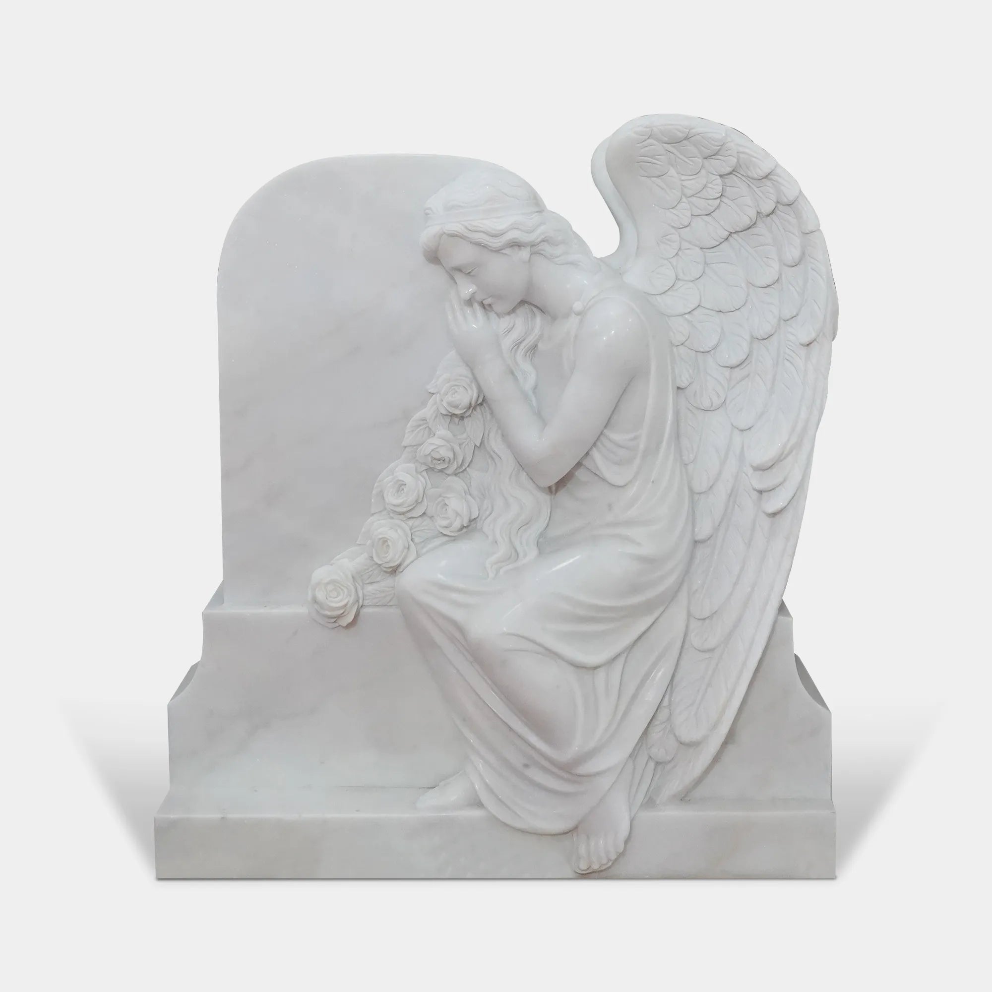 White marble angel statue leaning against a memorial marker in a cemetery garden, memorial setting