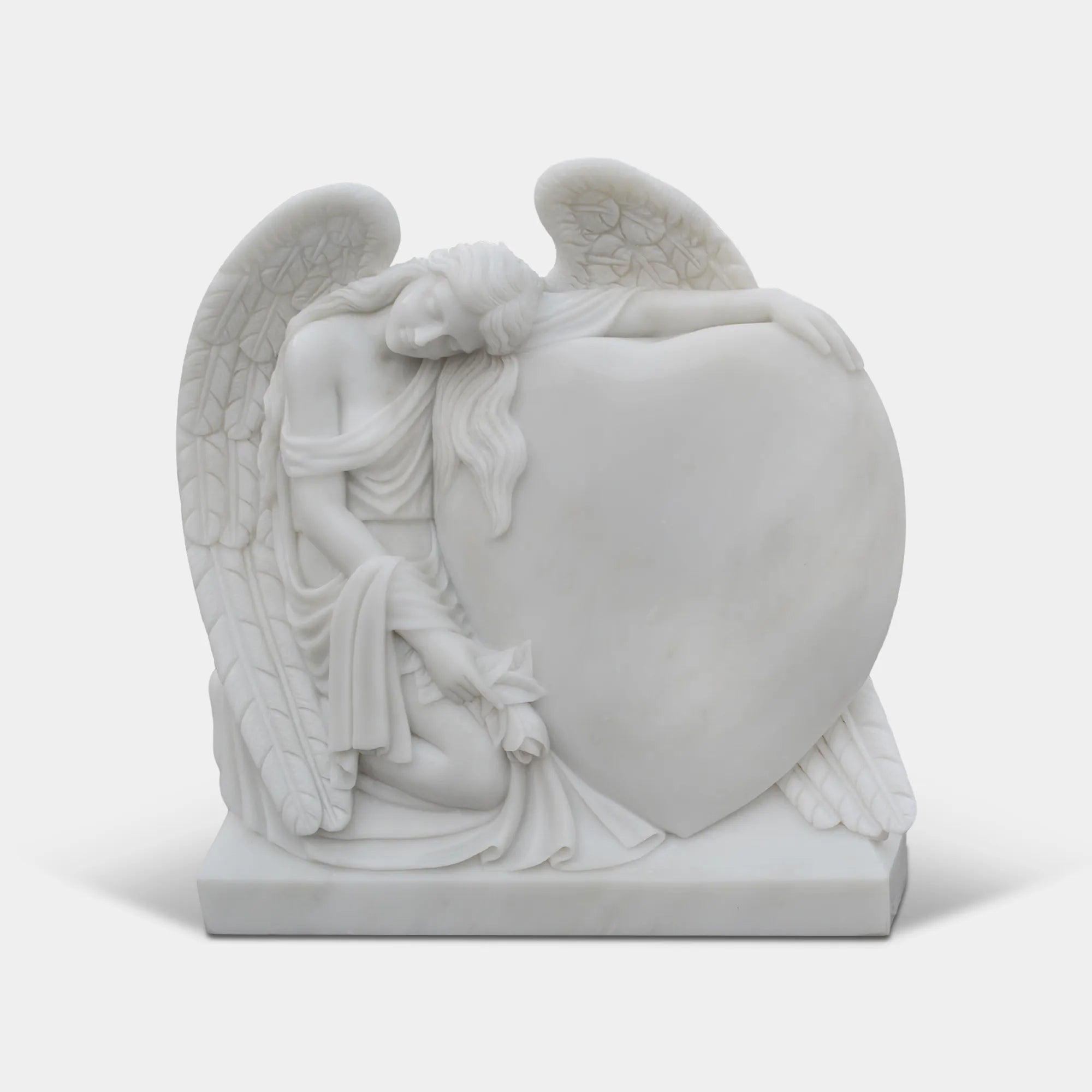 angel leaning on heart with closed eyes carved in white marble resting in cemetery memorial garden.