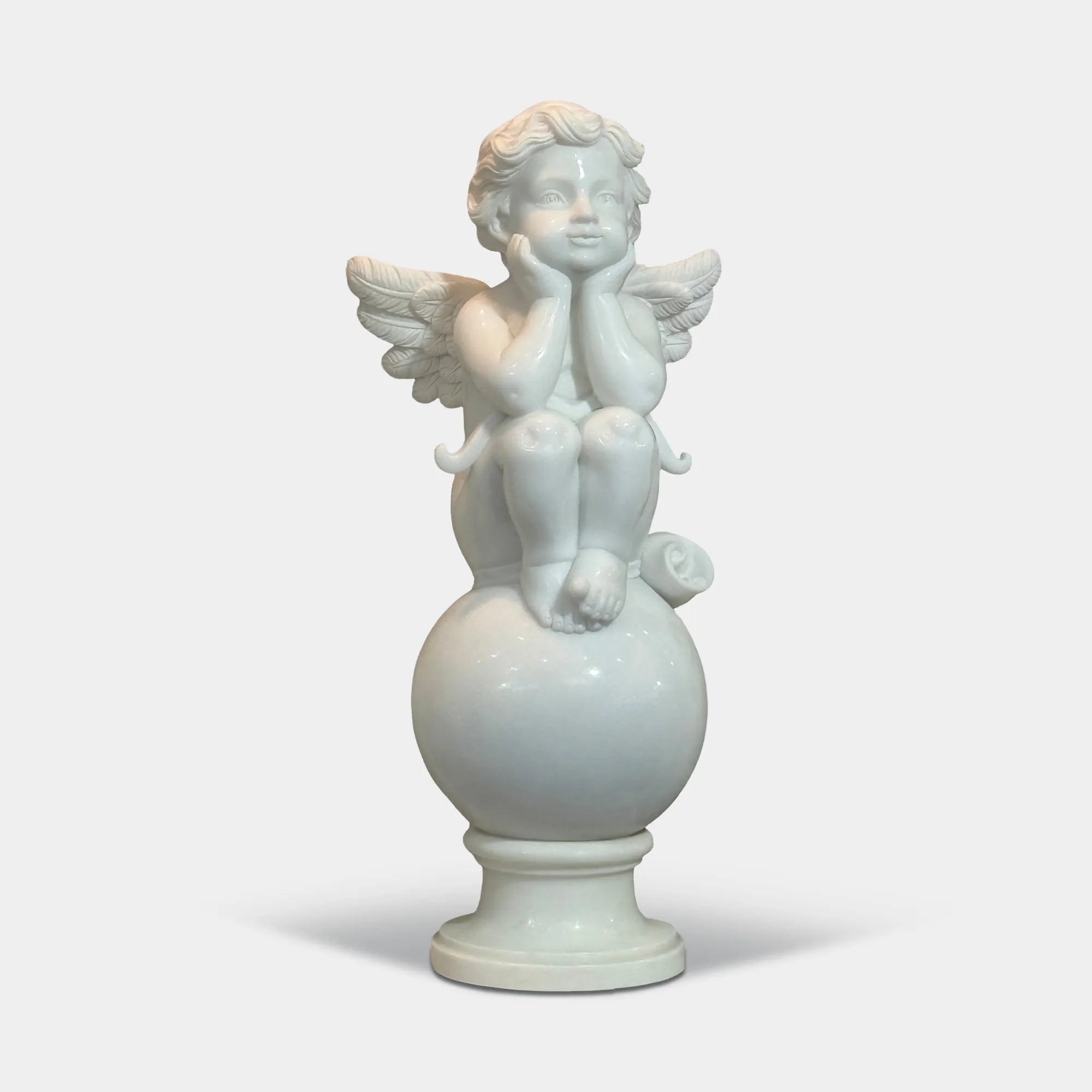 Angel cherub sitting with hands supporting face on a round stone pedestal carved in white marble in a pool center. 