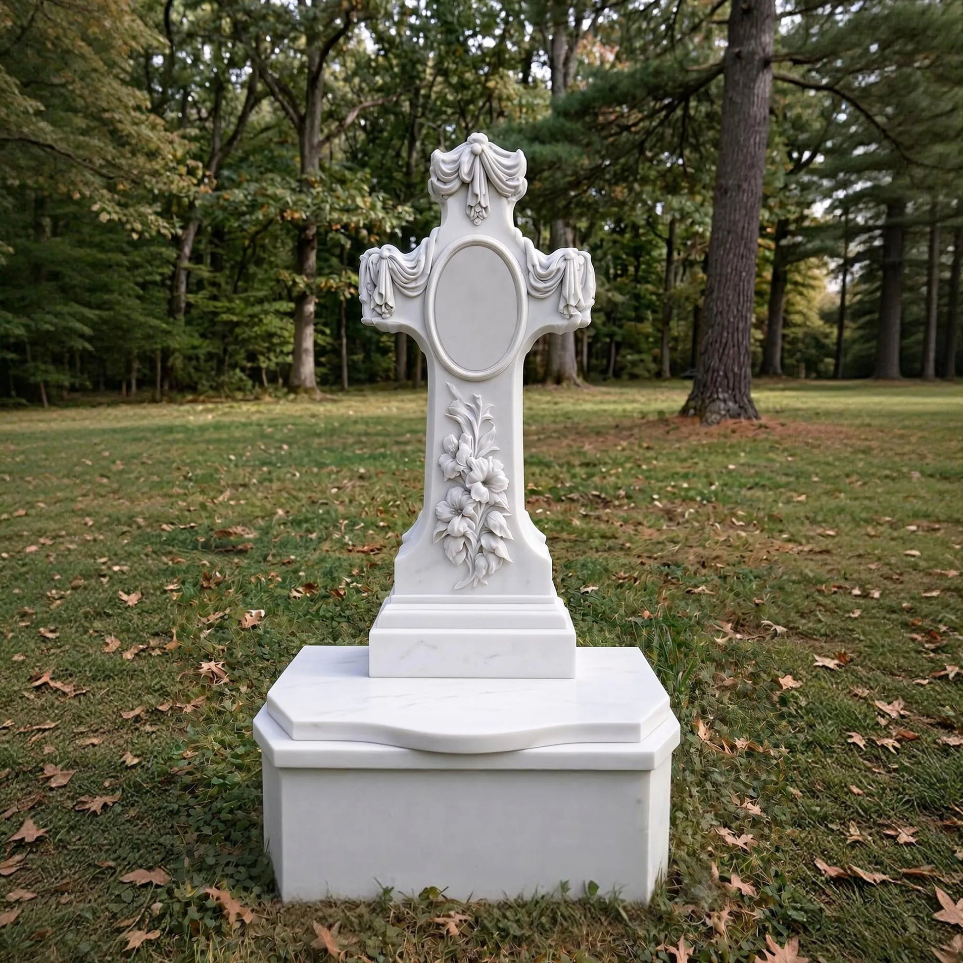 White marble memorial cross statue with floral relief carving and draped fabric details in cemetery memorial garden.