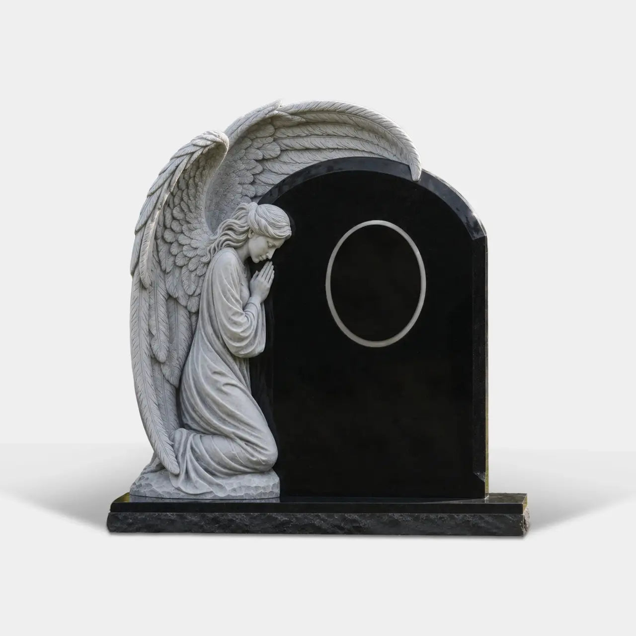 White praying angel marble statue attaches to black tombstone is placed on grassy cemetery lawn.