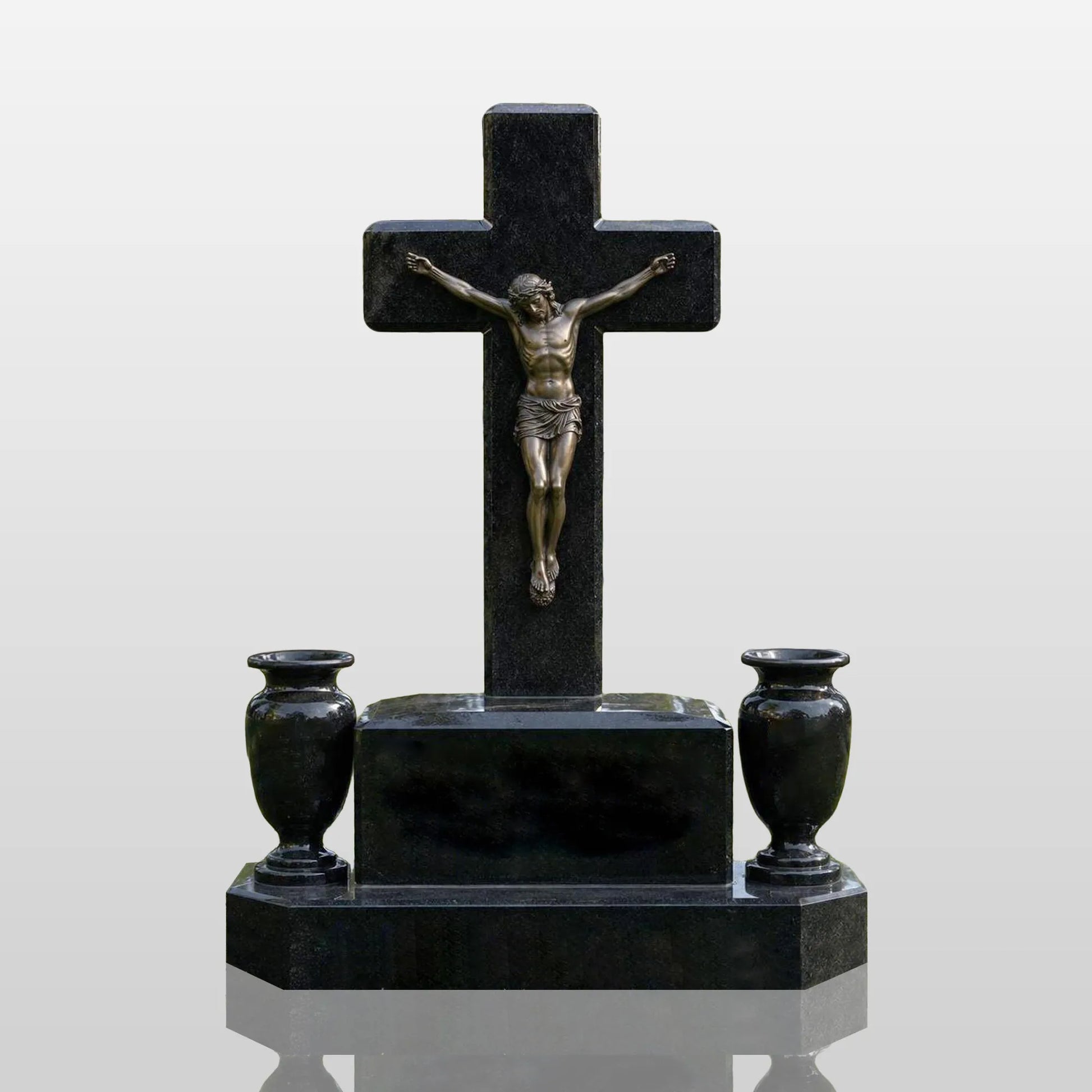 Black marble cross tombstone with bronze crucifix Jesus statue and two flower vases rests on green cemetery lawn.