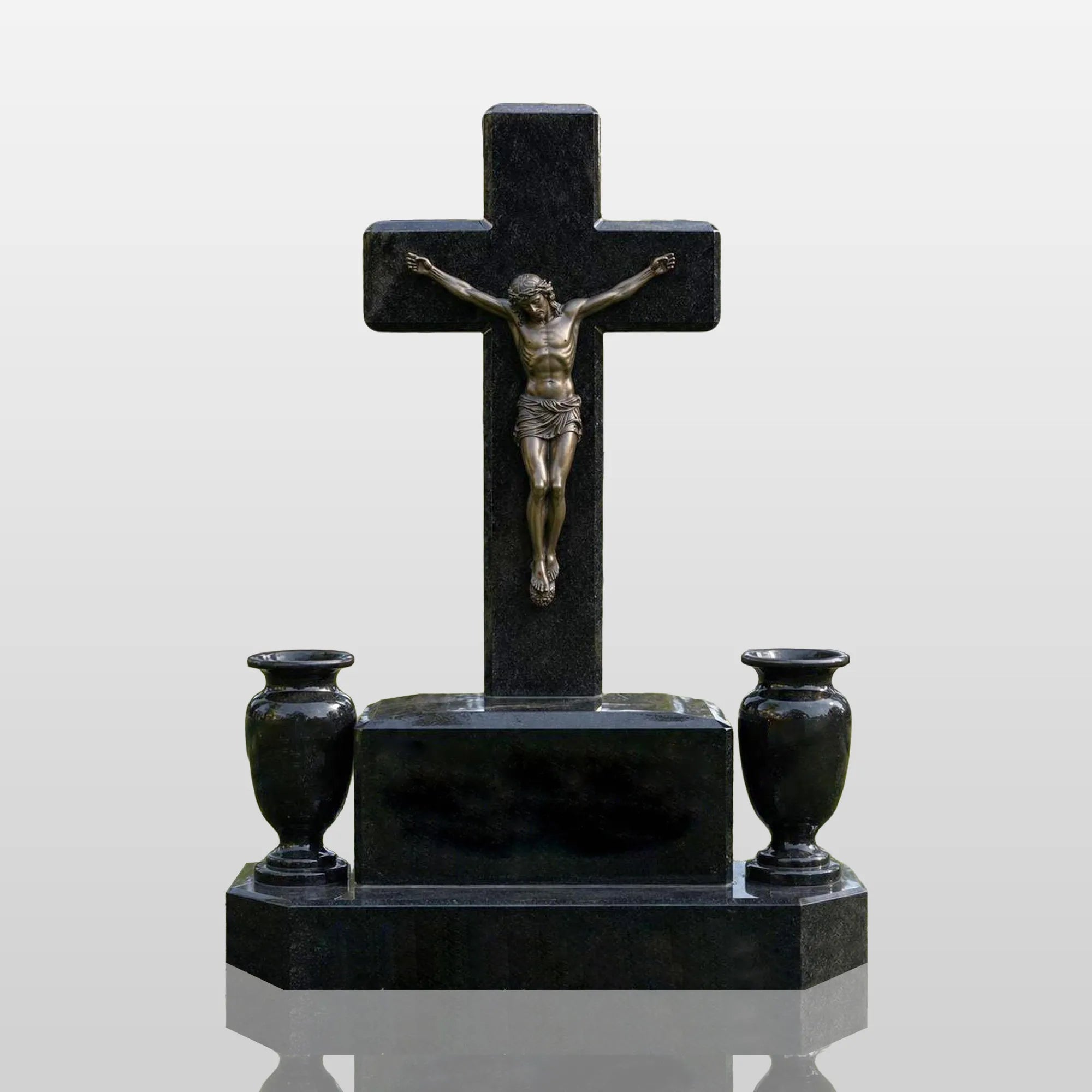 Black marble cross tombstone with bronze crucifix Jesus statue and two flower vases rests on green cemetery lawn.