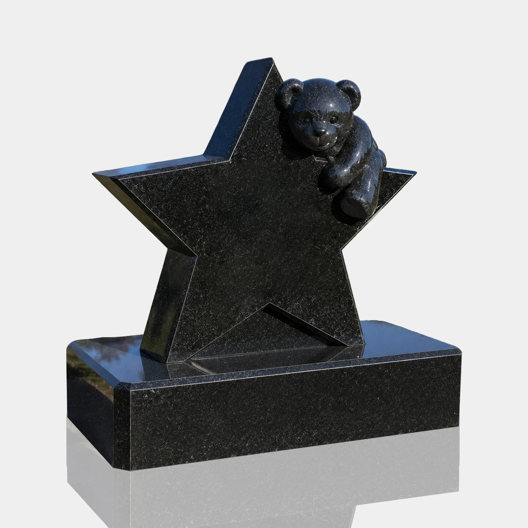Black marble tombstone with star and teddy bear rests on matching stone base on grassy cemetery ground.