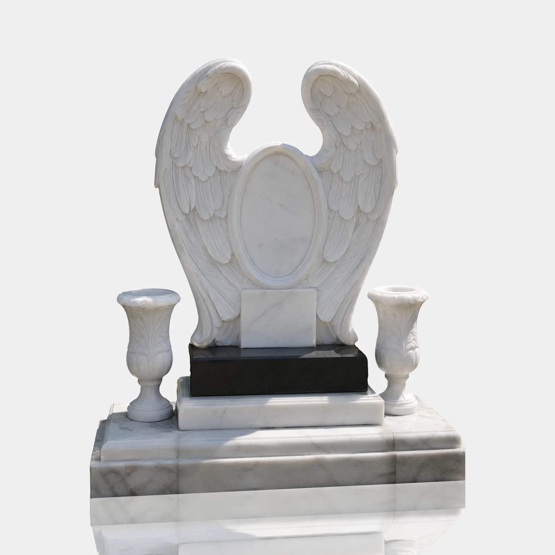 Marble wings headstone with two marble vases sits on layered stone plinth on cemetery pavement.