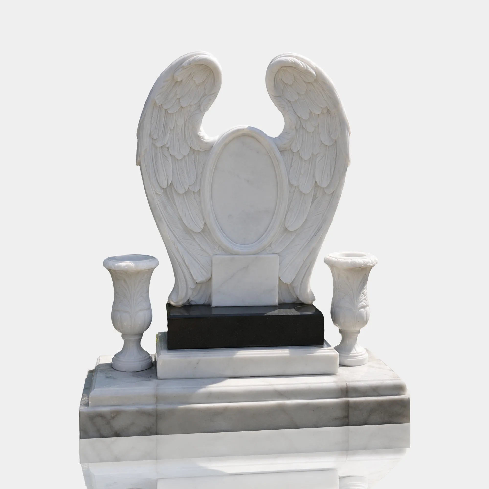 Marble wings headstone with two marble vases sits on layered stone plinth on cemetery pavement.