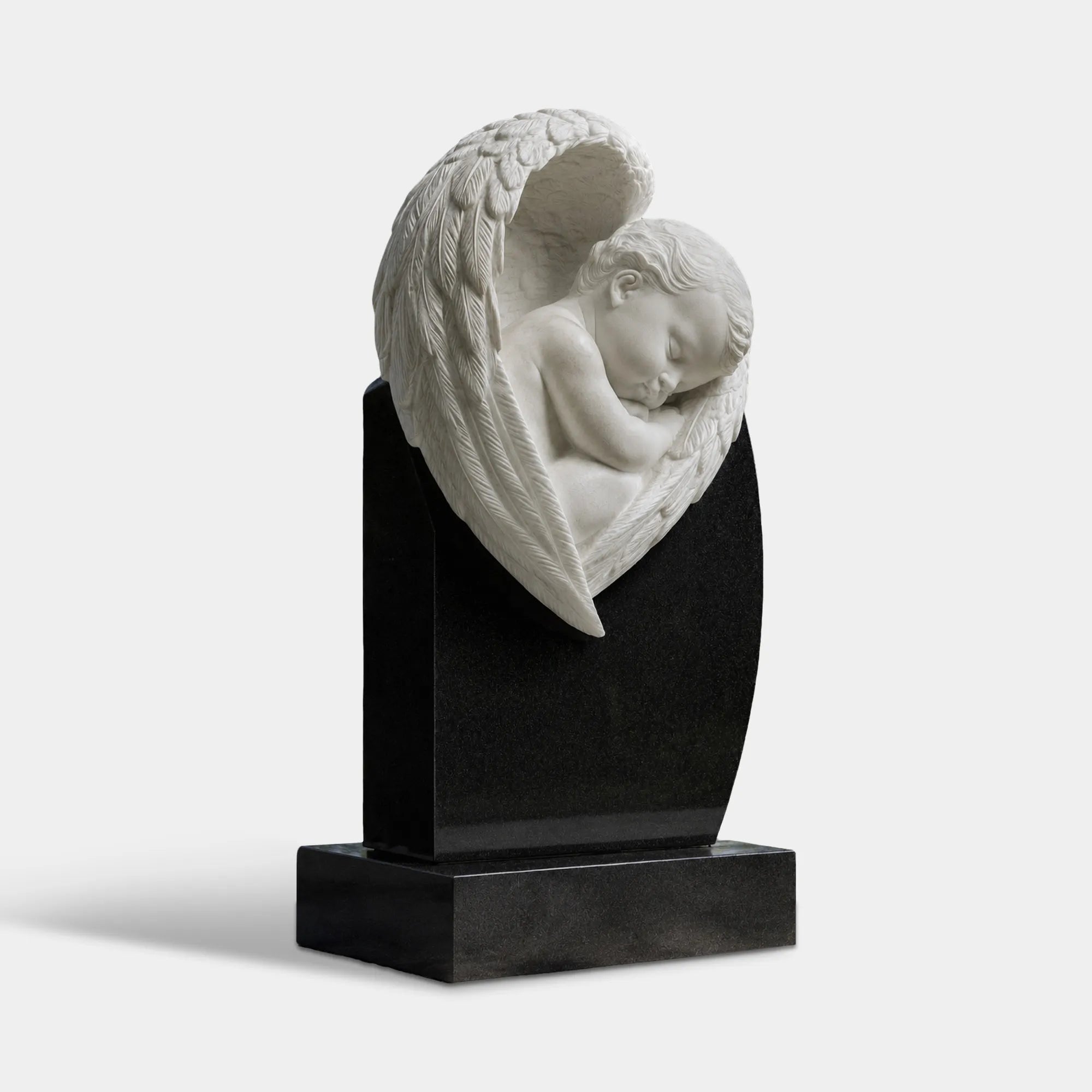 White marble sleeping child angel sculpture with one large wing mounted on a polished black marble headstone in a cemetery walkway.