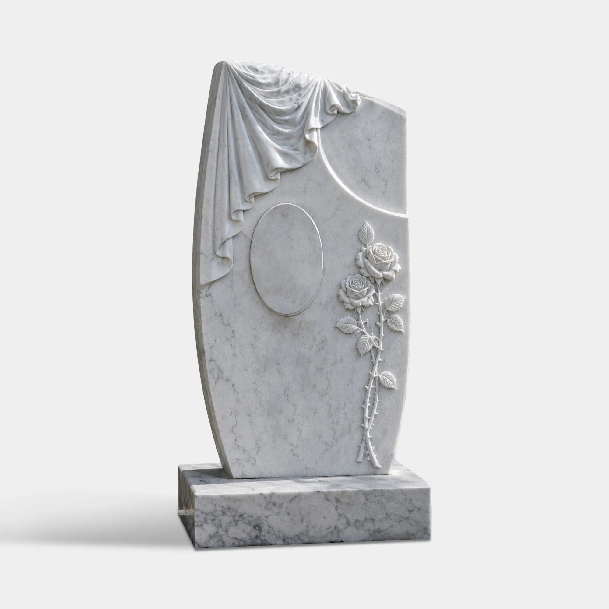 White marble headstone with carved draped cloth, oval center detail, and rose relief on a rectangular base in a cemetery garden.