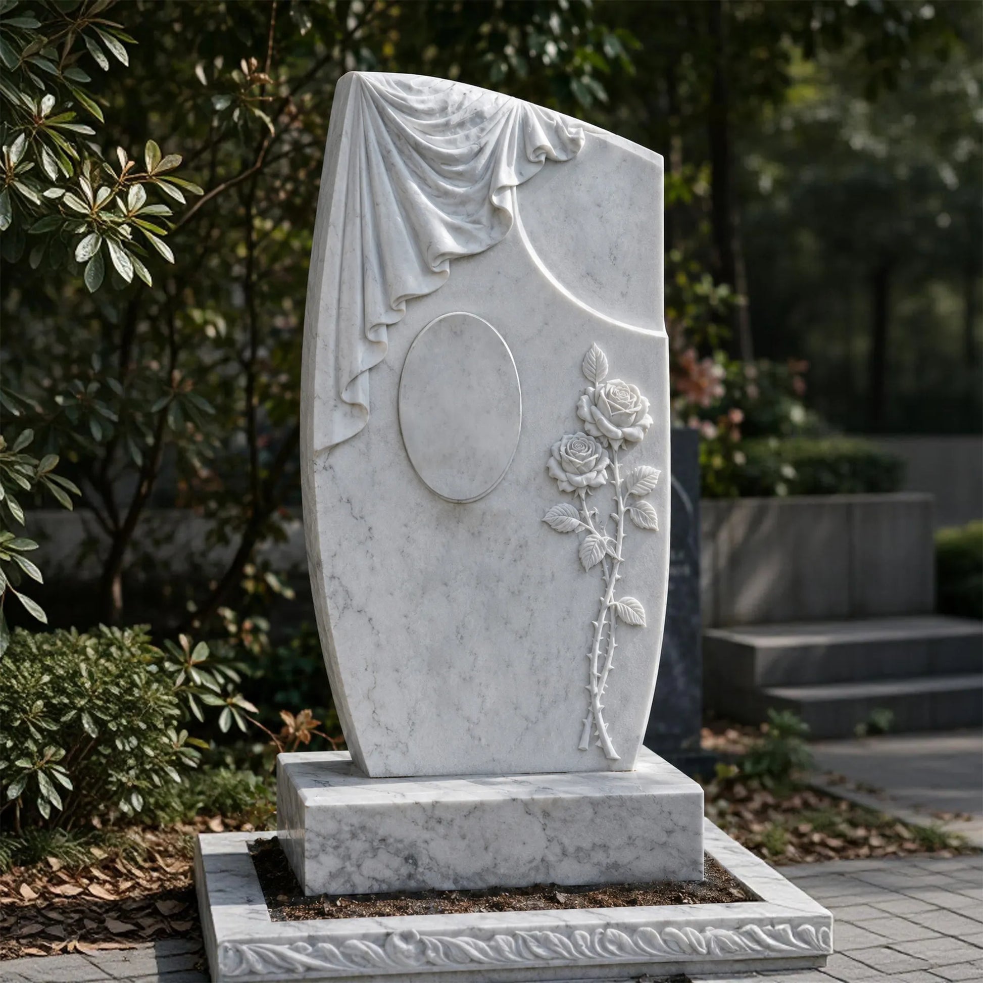 White marble headstone with carved draped cloth, oval center detail, and rose relief on a rectangular base in a cemetery garden.