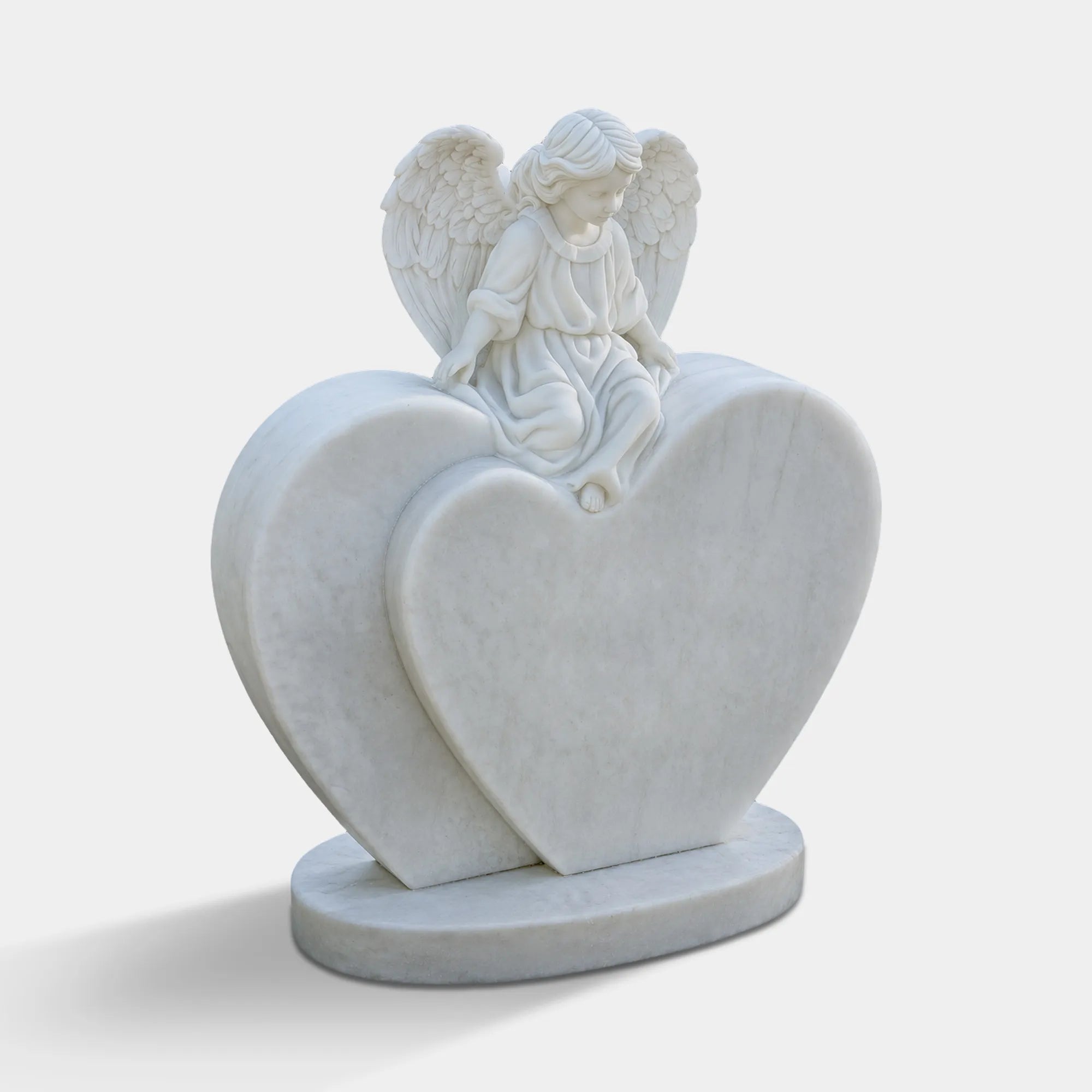 White marble angel statue seated on a layered heart-shaped memorial base in a cemetery walkway.