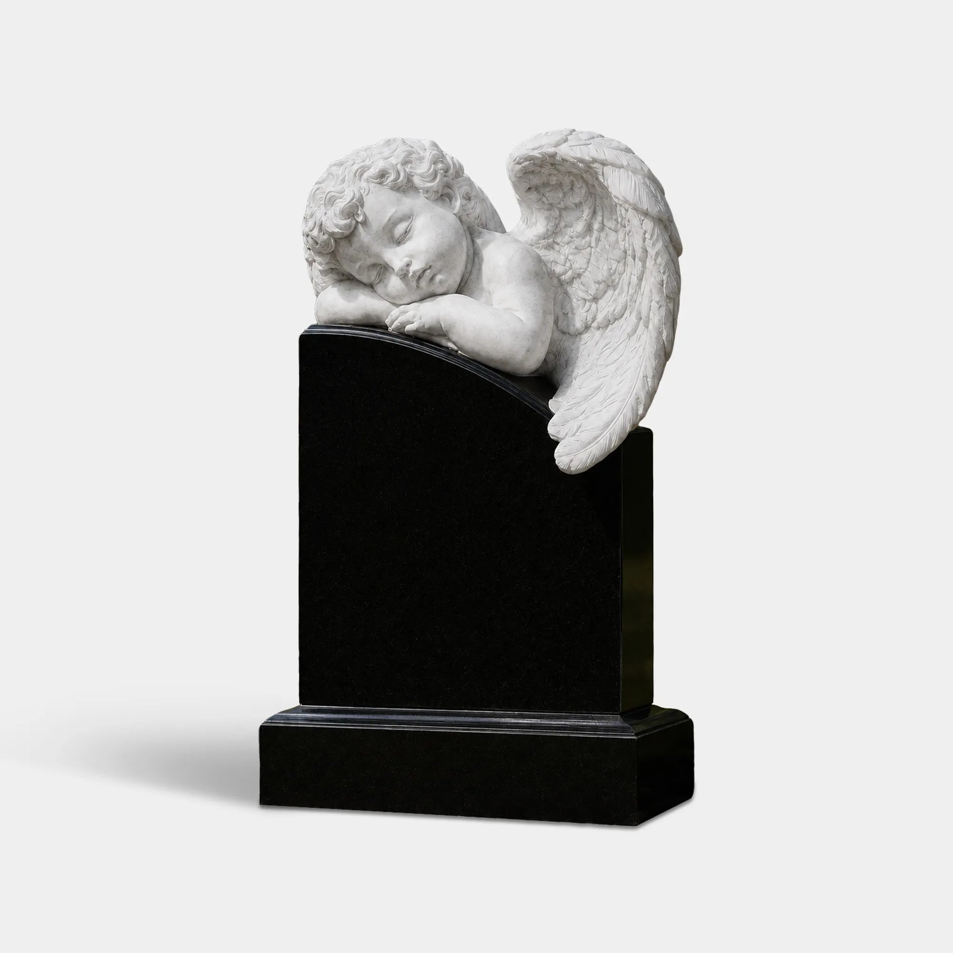 White marble sleeping angel statue on a black marble headstone in a cemetery garden.