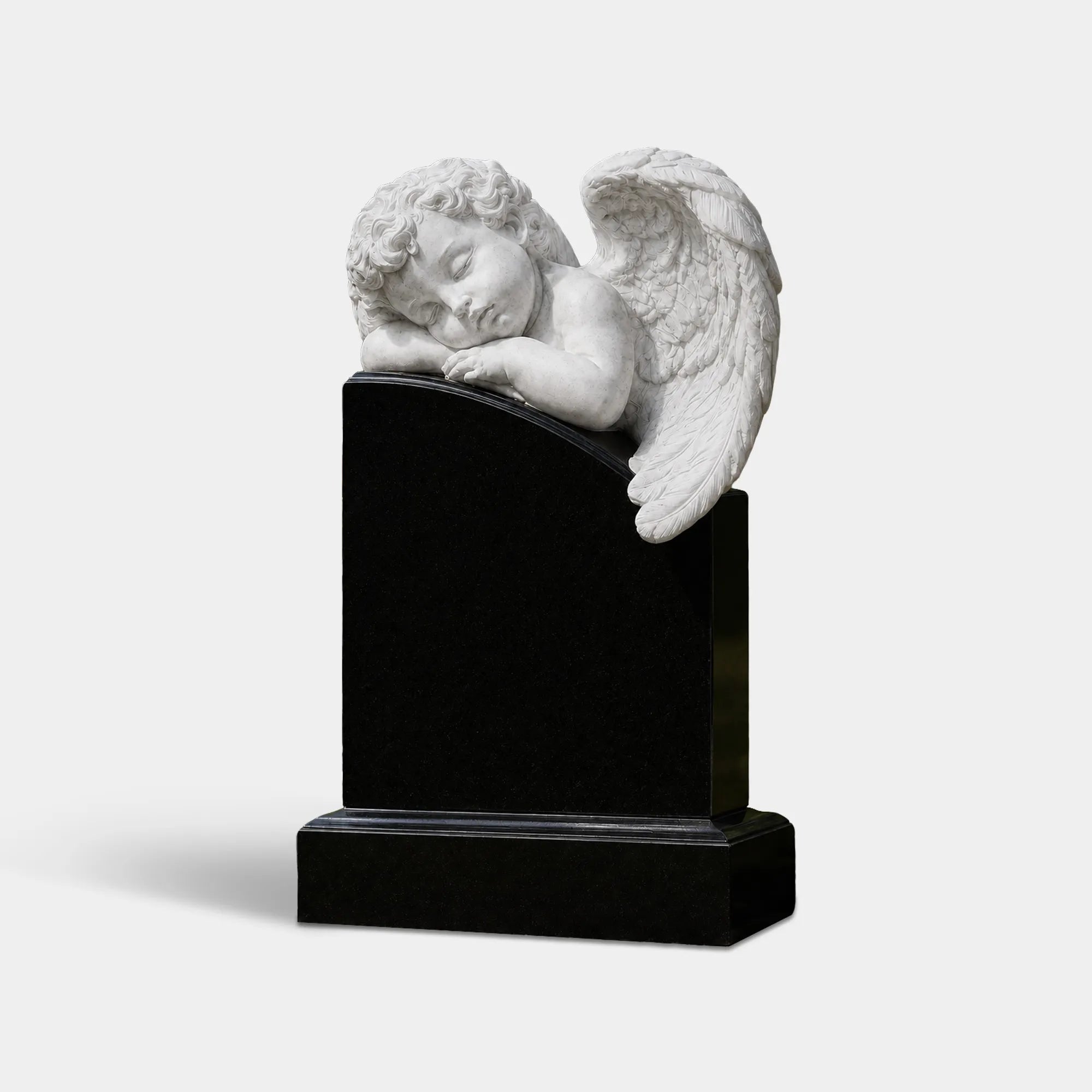 White marble sleeping angel statue on a black marble headstone in a cemetery garden.