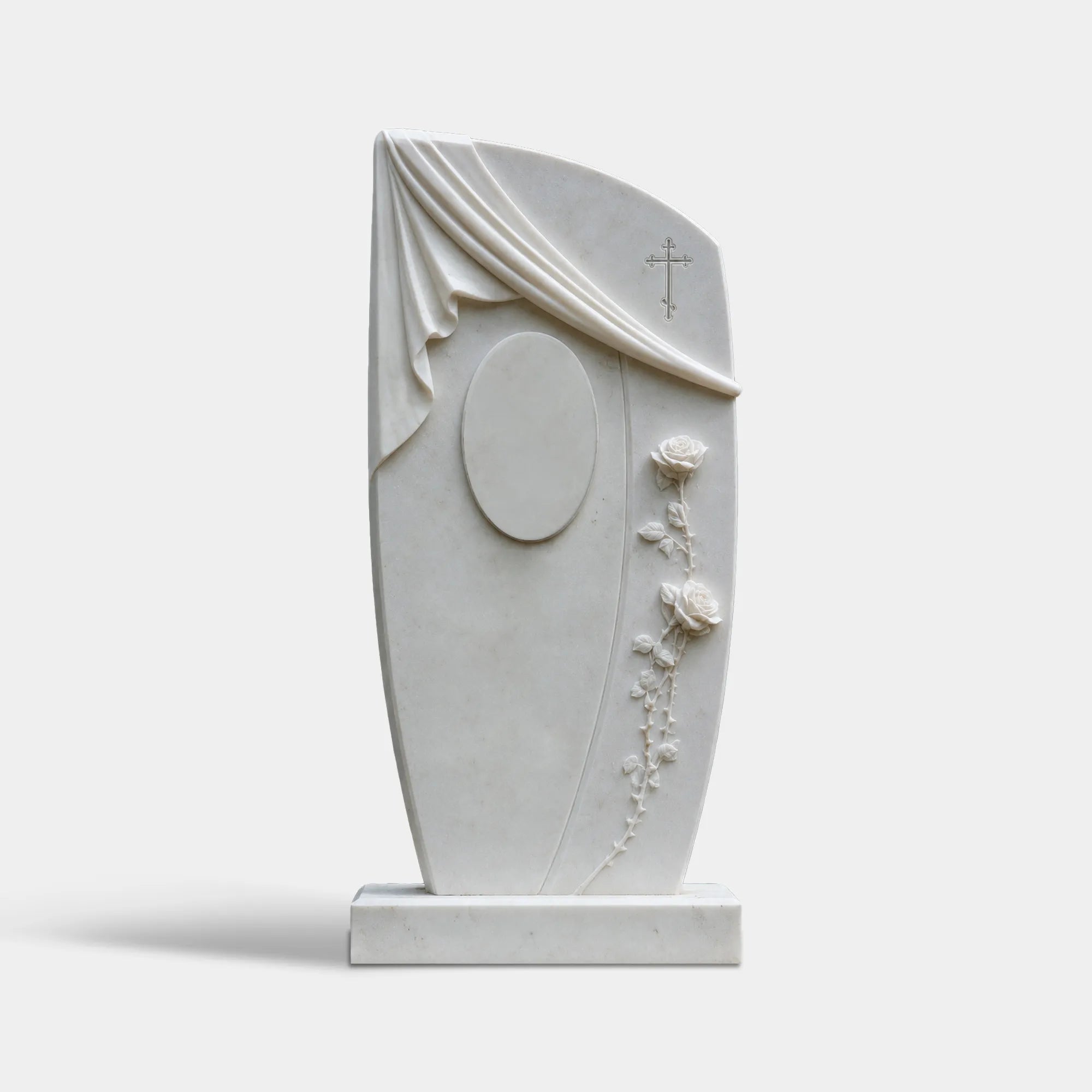 Curved white marble headstone carved with drape and roses sits on on mulched cemetery ground.