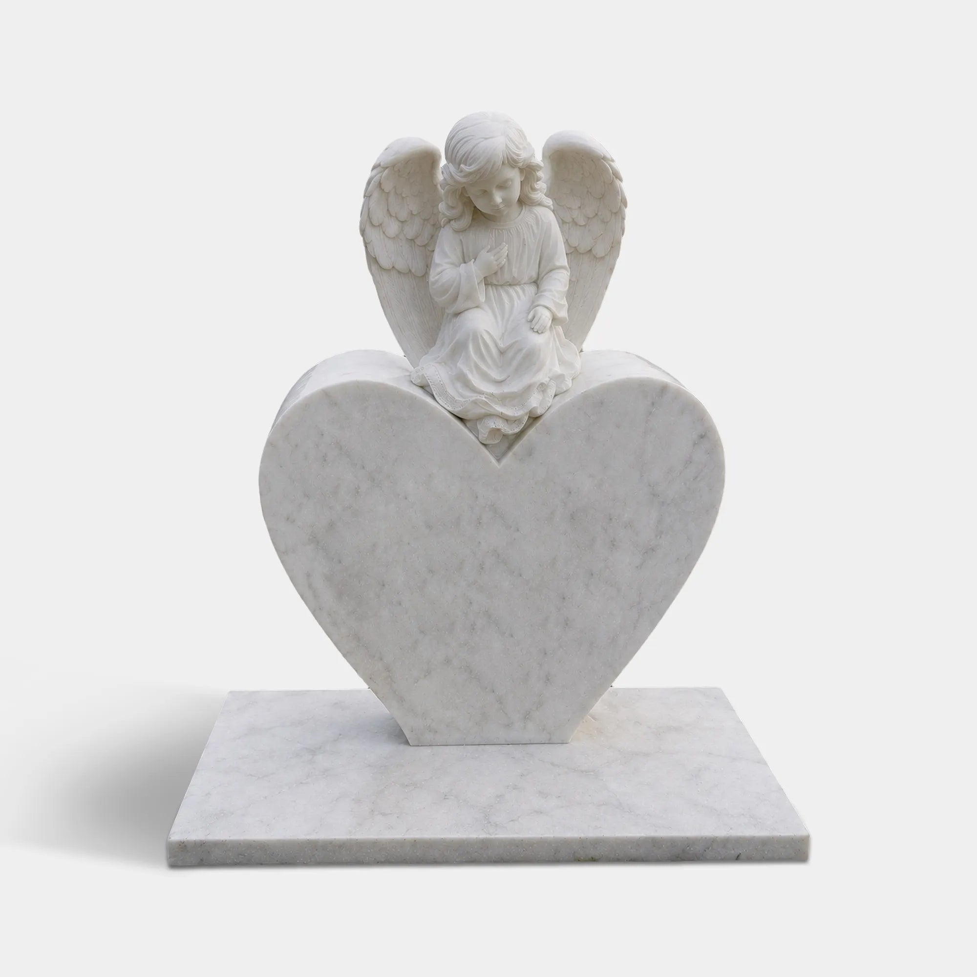 Heart shaped marble tombstone carved with angel stands on grassy cemetery ground.