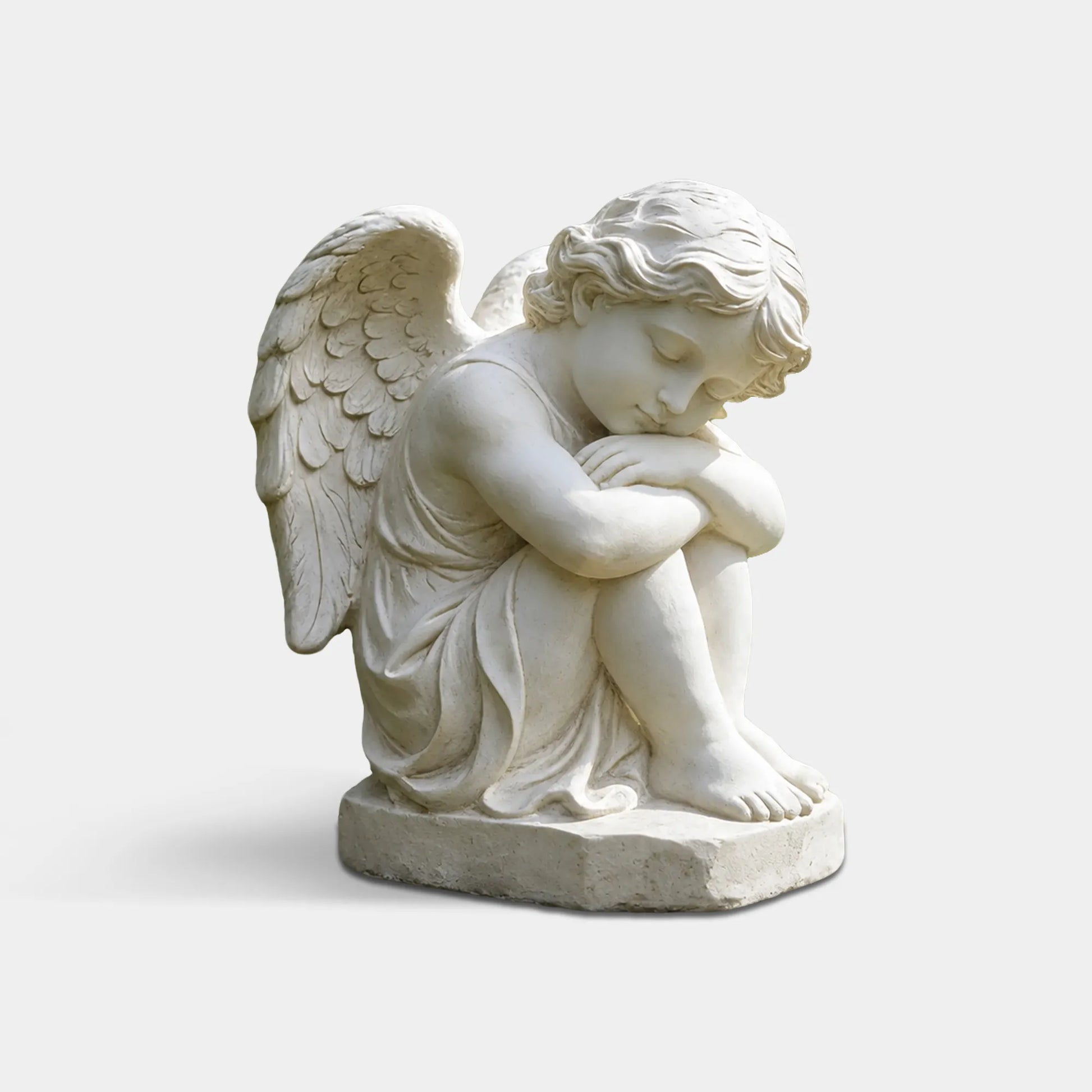 A marble sleeping cherub statue rests on a stone ledge within a quiet graveyard.