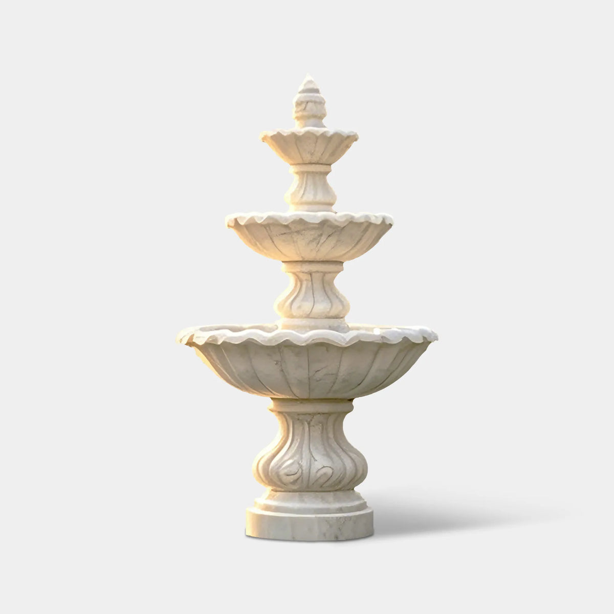 White marble three-tier fountain with scalloped basins in a pool garden beside stone walls and a hillside villa.
