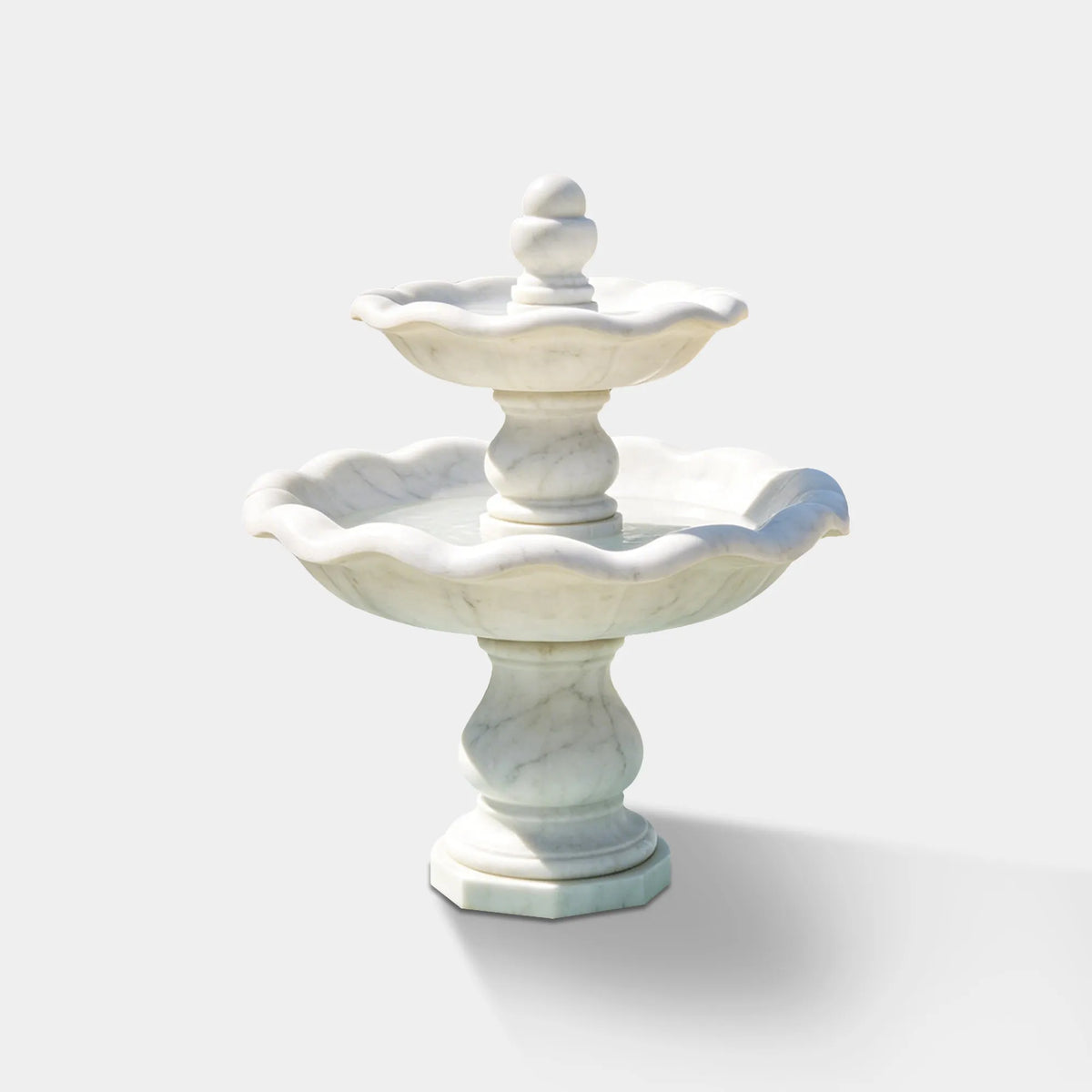 White marble two-tier fountain in a paved residential courtyard beside a villa.
