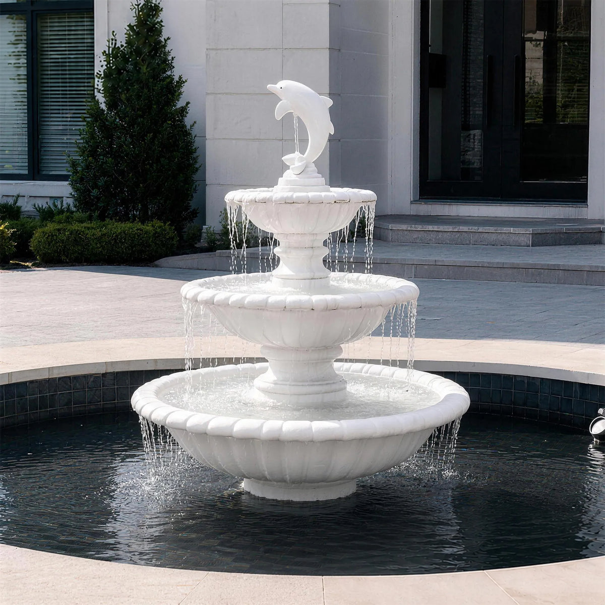 A three tier marble fountain with dolphin statue sits in a circular basin outside a residential home.