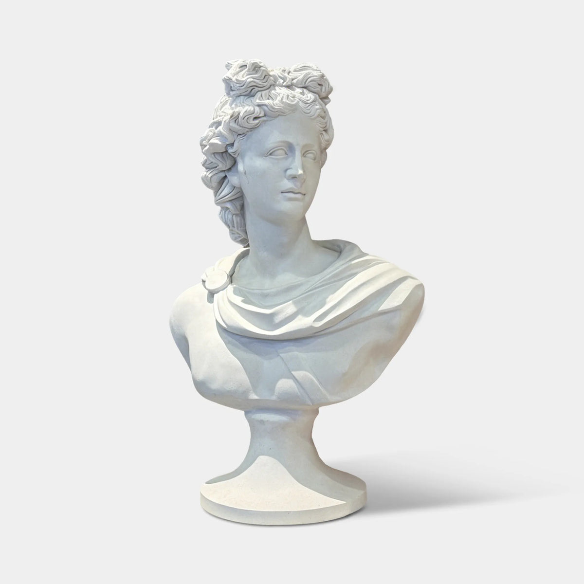 A marble Apollo bust rests on a round side table with candle decorations in a vintage room.