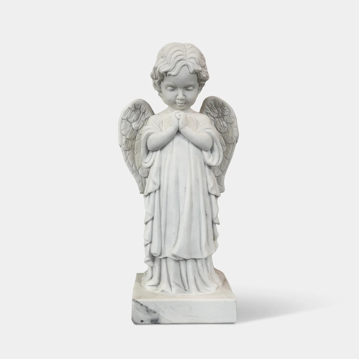 A marble praying cherub statue stands on an ornate pedestal in a formal European garden.
