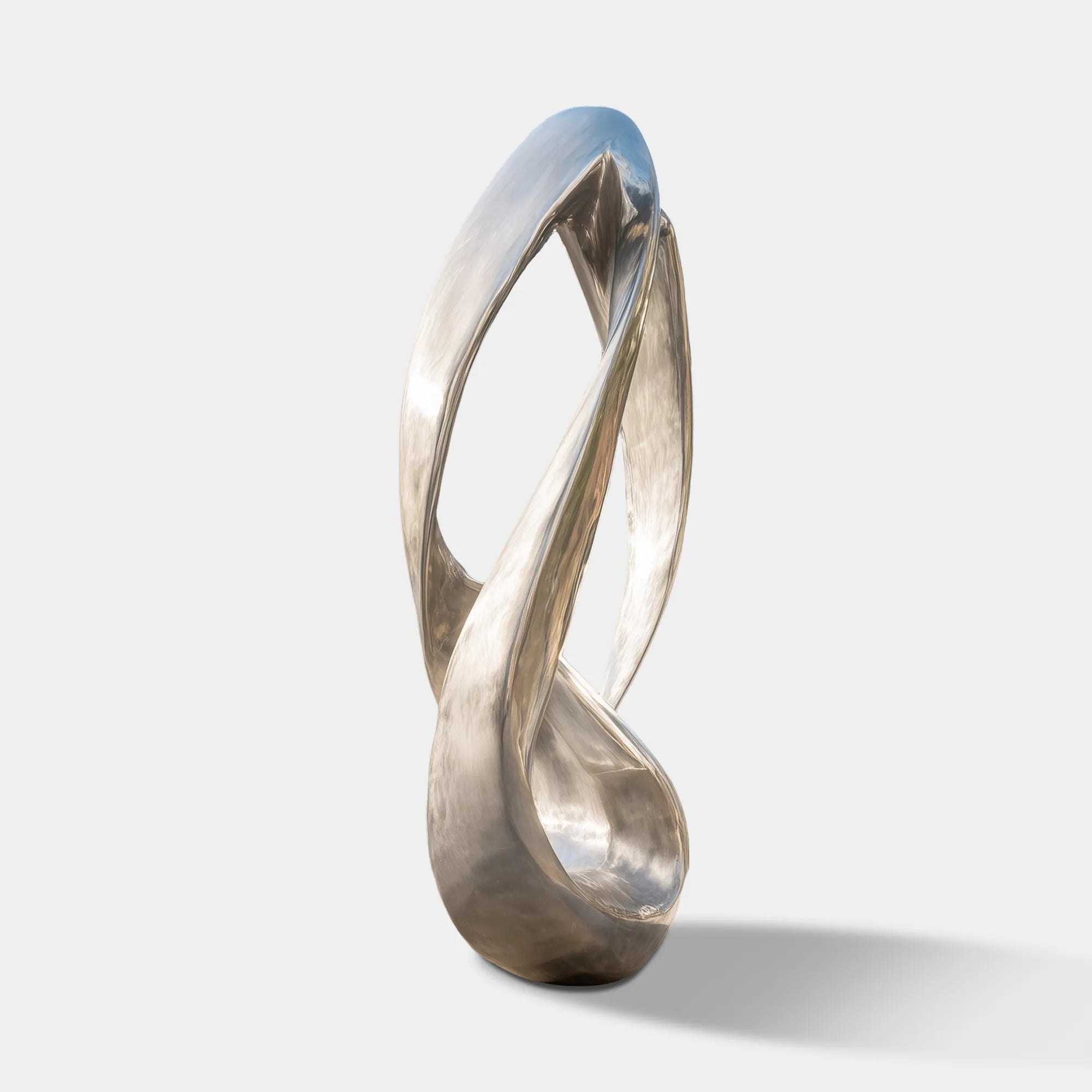 Brushed stainless steel abstract loop sculpture on concrete base in front of glass modern villa surrounded by trees