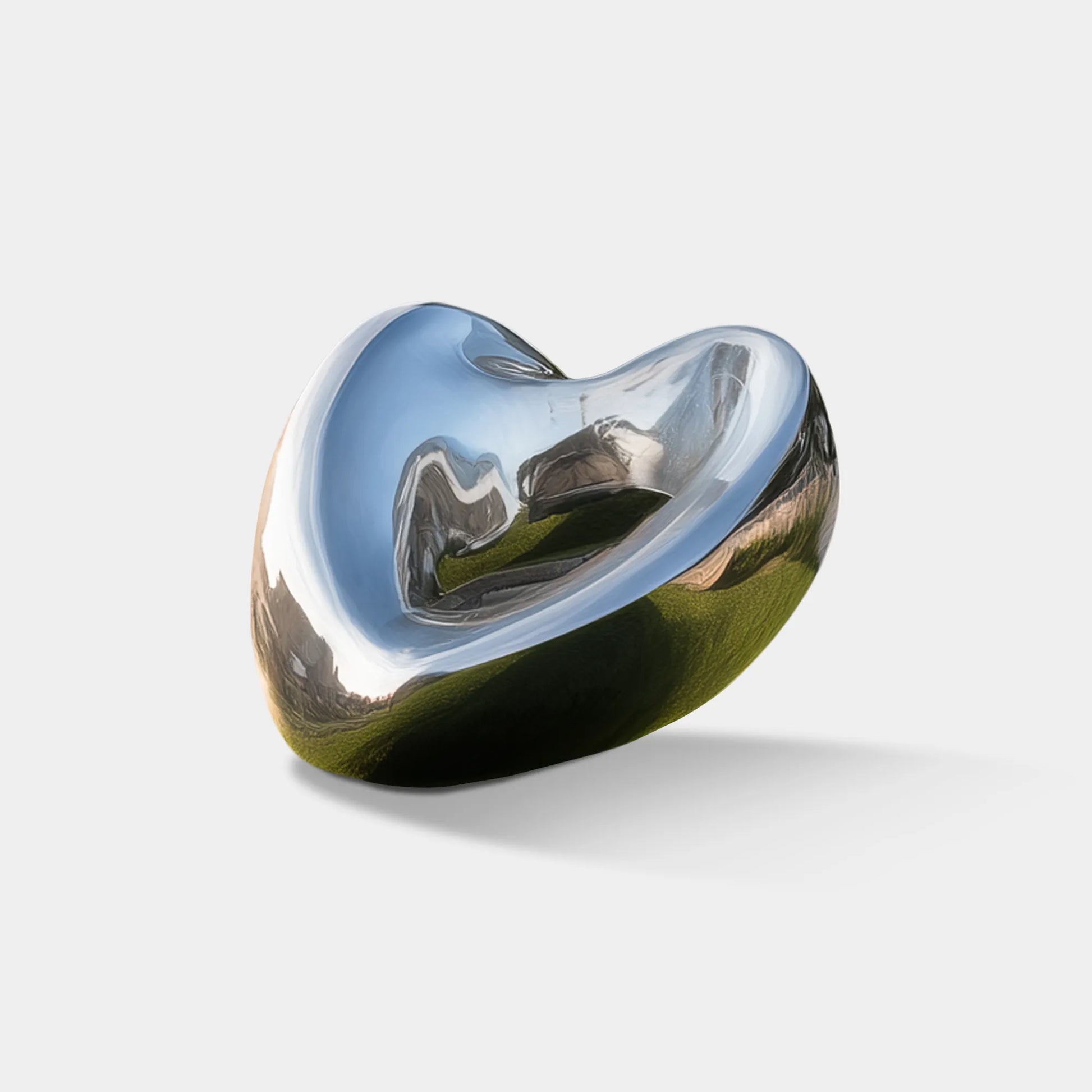 Polished stainless steel sculpture in heart shape on grass in front of a villa.