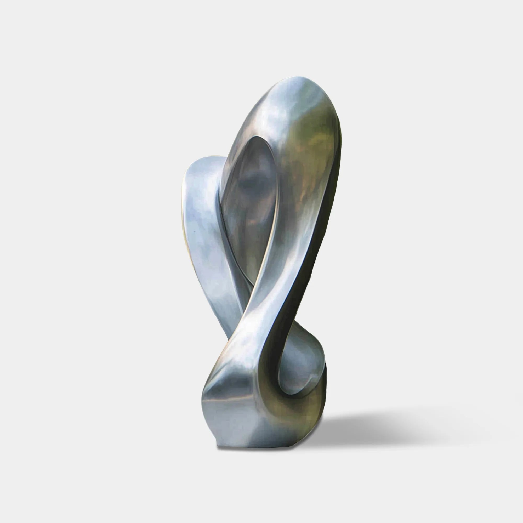 Figure eight inspired stainless steel abstract sculpture with flowing loop form beside modern glass house exterior and green trees.