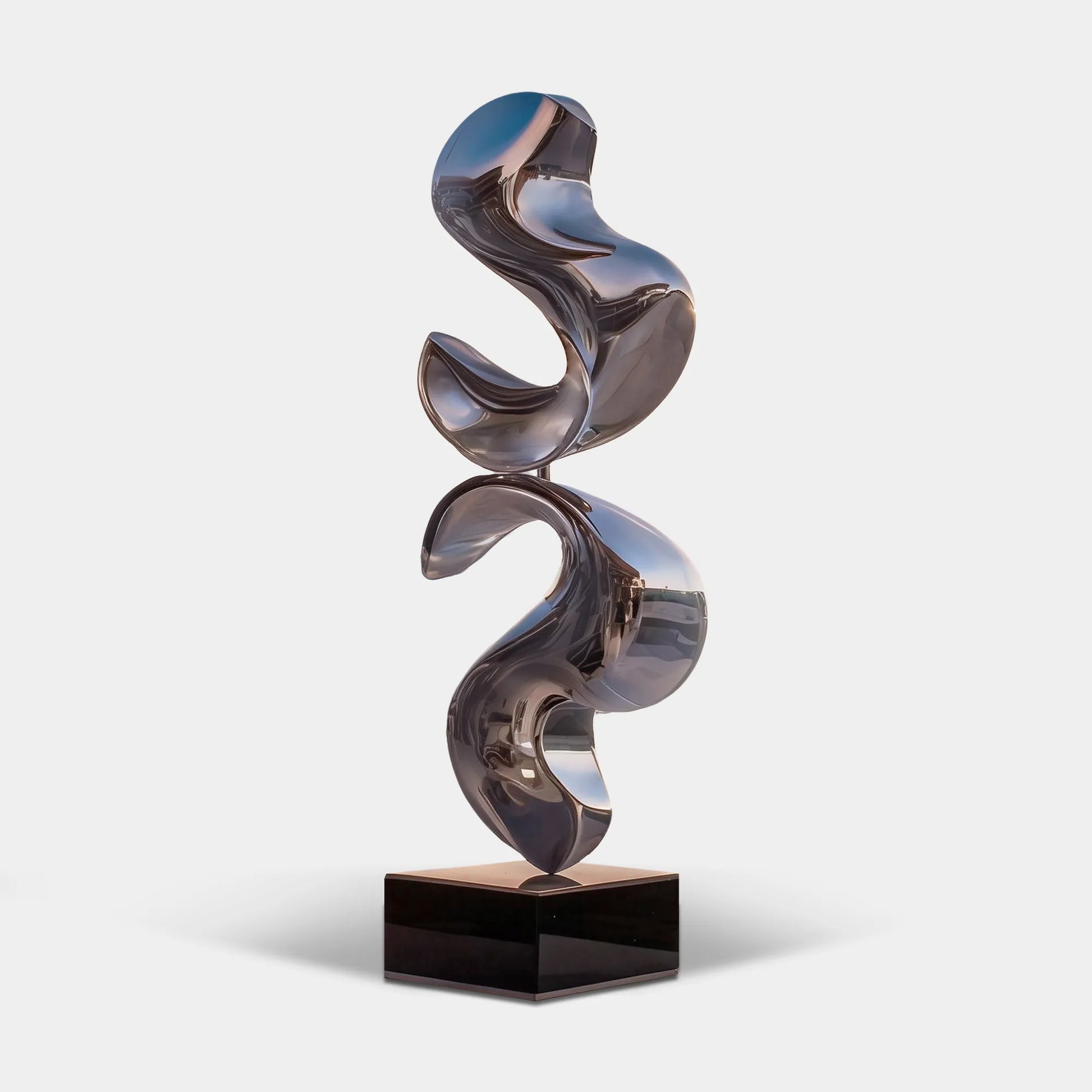 Polished stainless steel abstract sculpture on a black pedestal overlooking a coastal waterfront terrace.