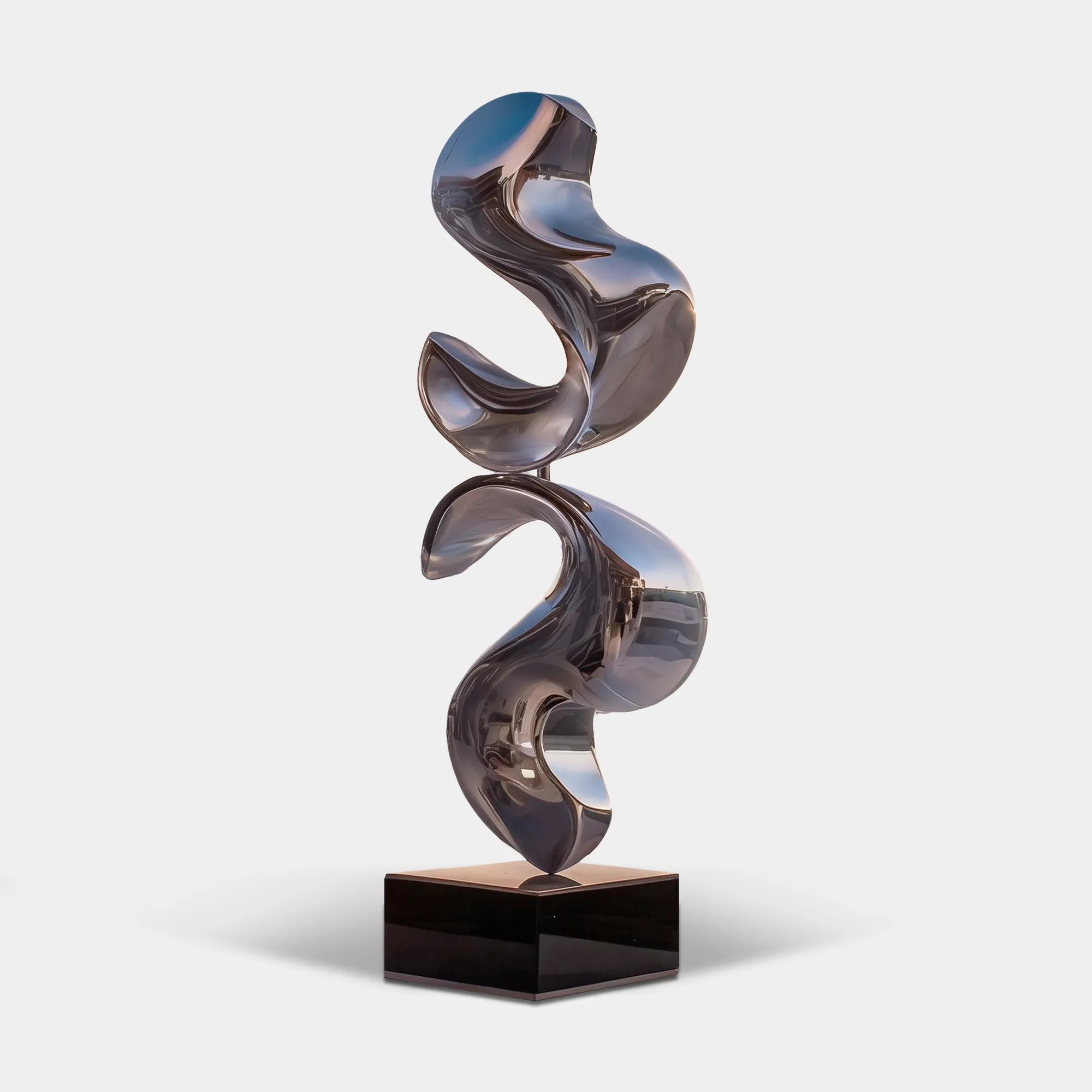 Polished stainless steel abstract sculpture on a black pedestal overlooking a coastal waterfront terrace.