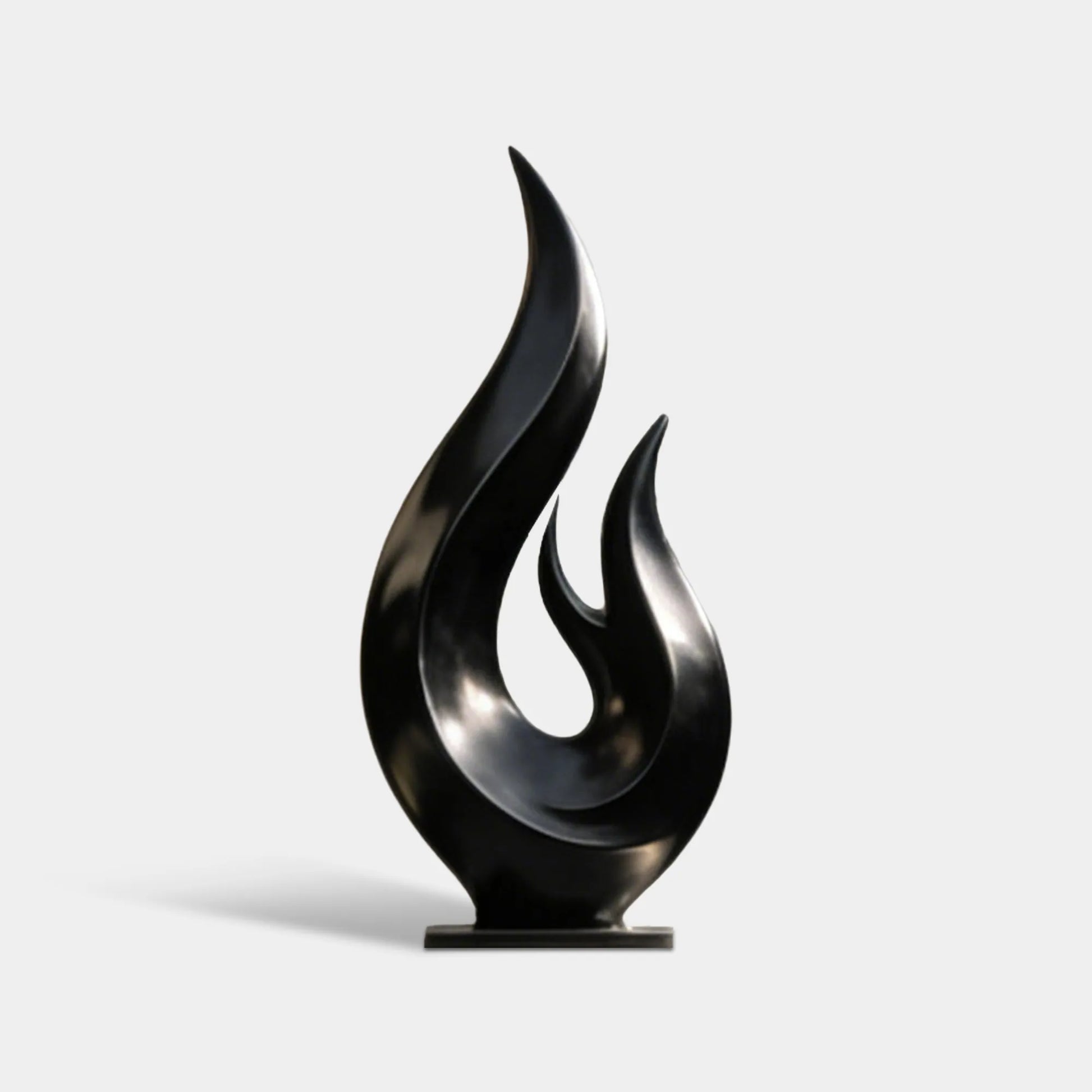 Black flame stainless steel sculpture stands on green lawn against light stone wall.