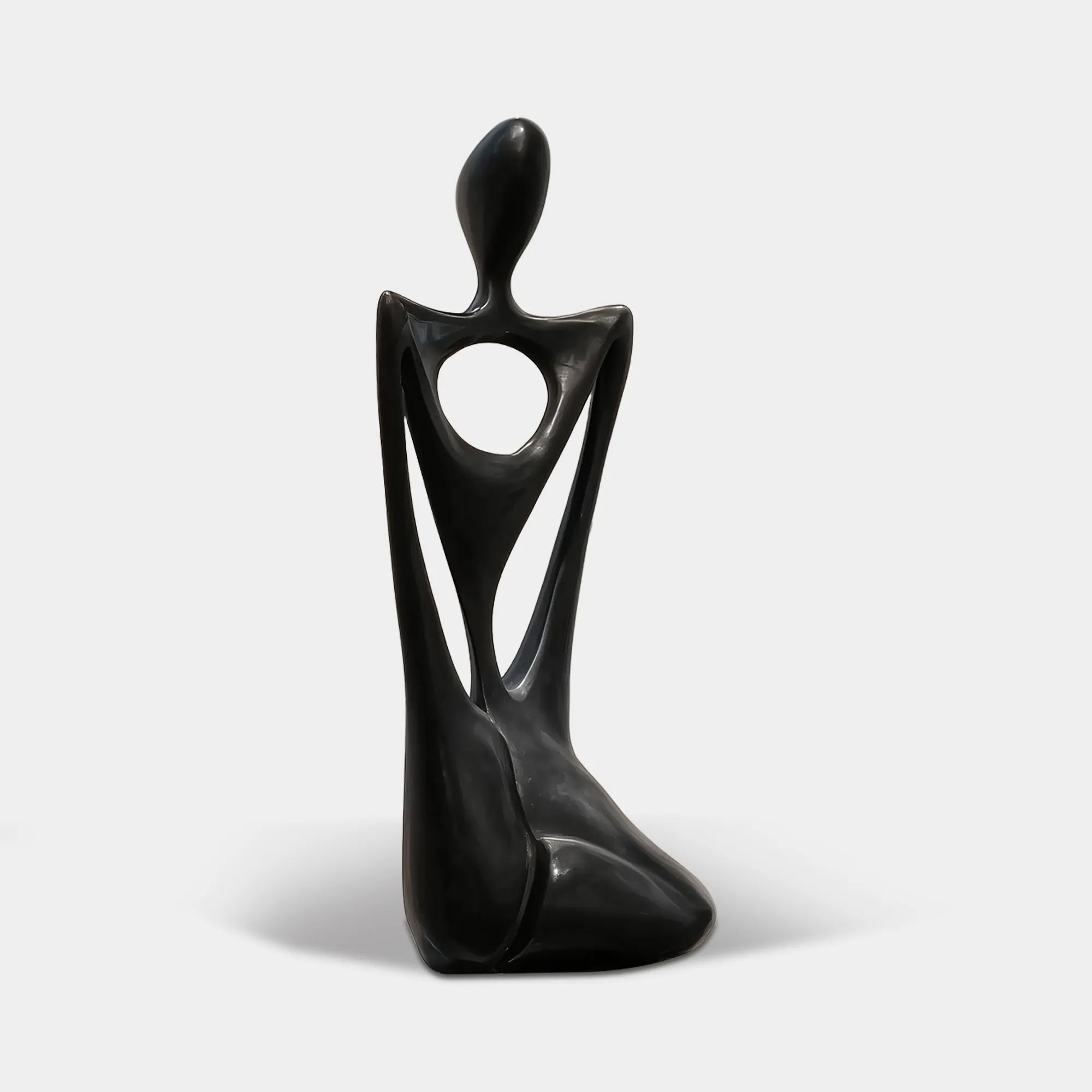 A black hollow abstract seated figure stainless steel sculpture rests beside a lit concrete staircase and sheer curtains.