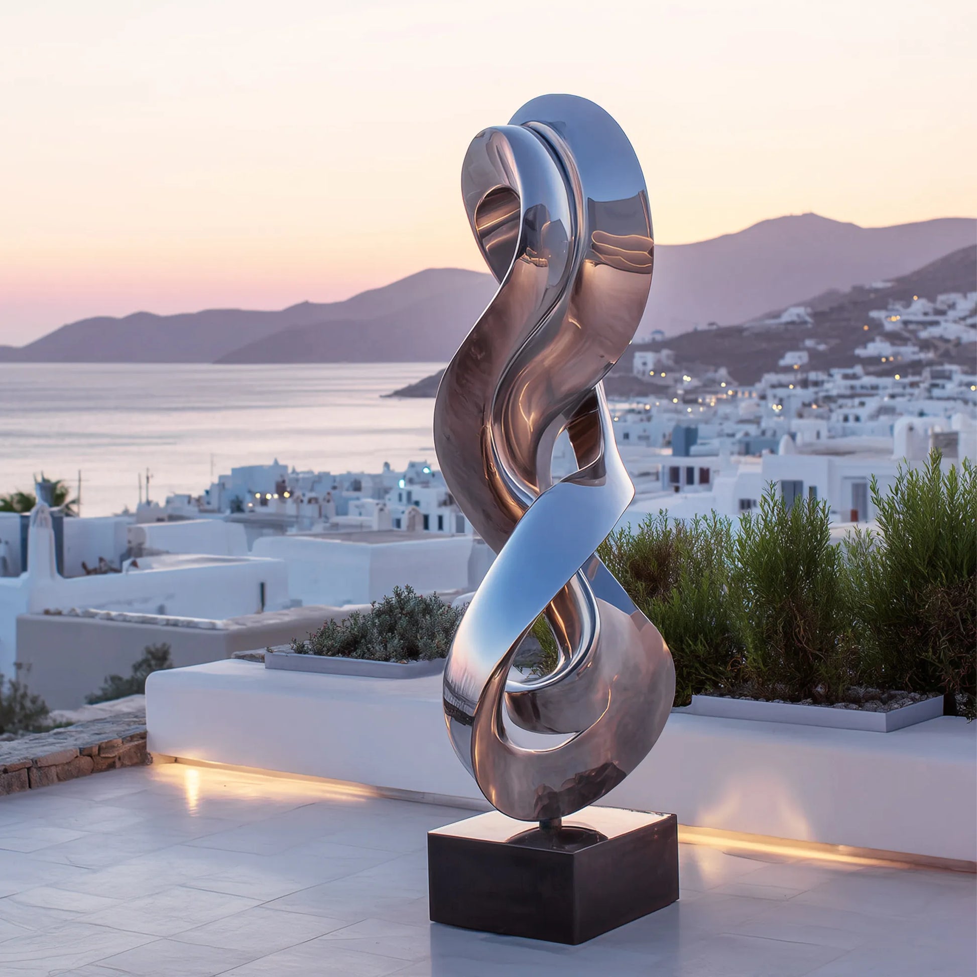 Mirror twisted curve stainless steel sculpture stands on tiled rooftop terrace overlooking coastal white town.