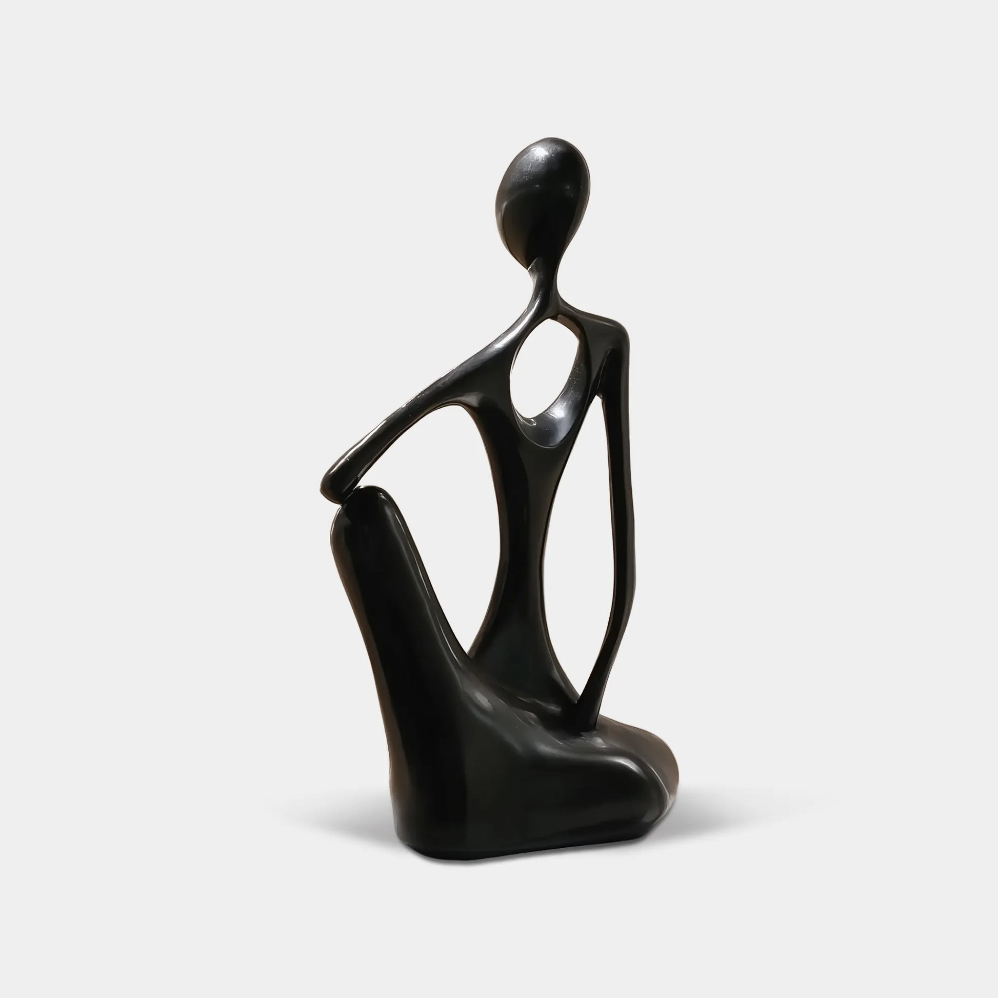 Black abstract stainless steel seated human sculpture on a stone pedestal beside a floor-to-ceiling window in a modern interior