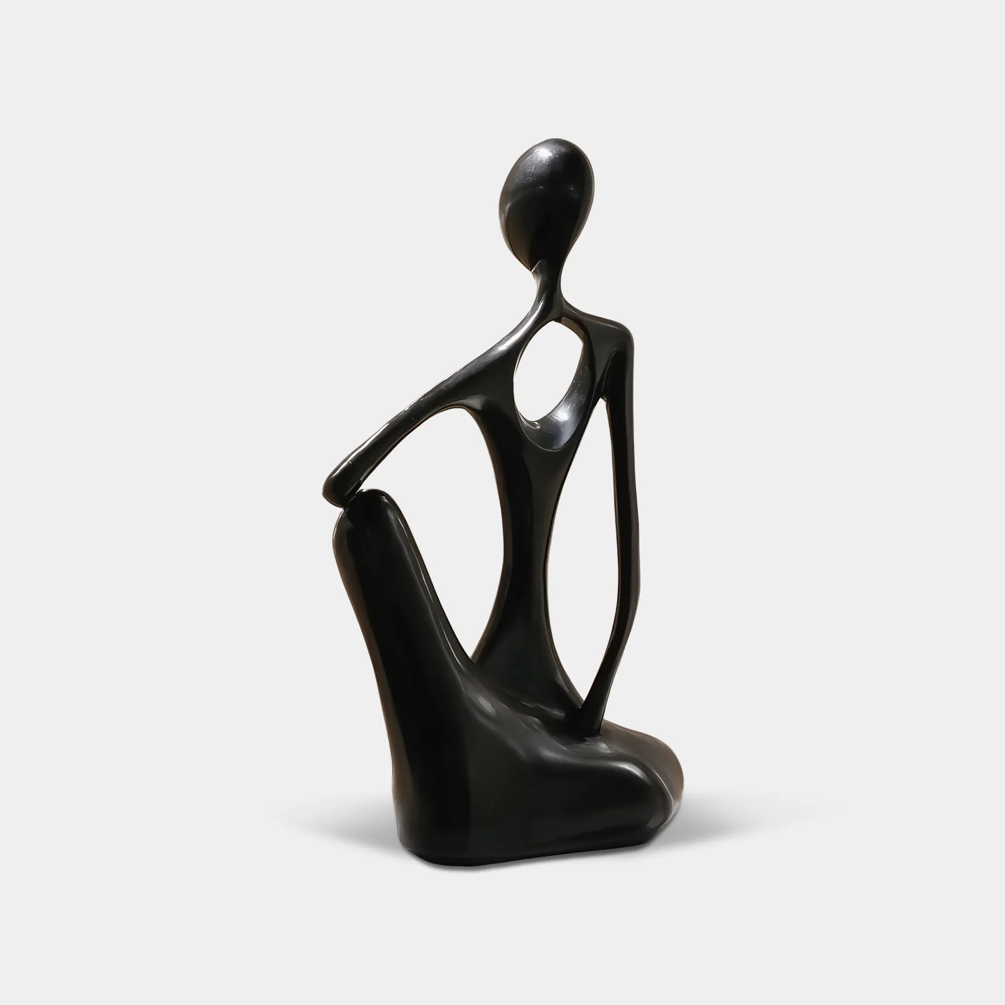 Black abstract stainless steel seated human sculpture on a stone pedestal beside a floor-to-ceiling window in a modern interior