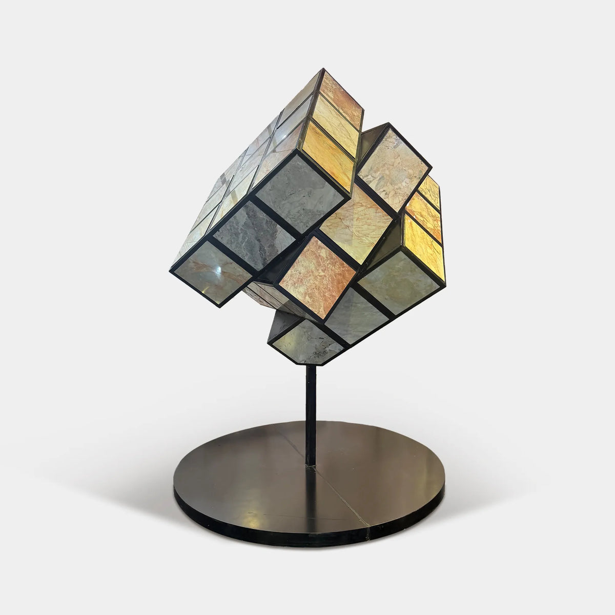 Geometric cube sculpture with natural stone panels inset into stainless steel frames on a round base in a luxury high-rise interior