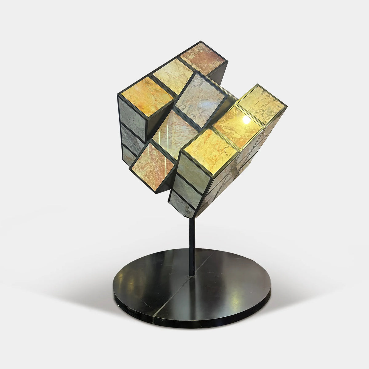 Geometric cube sculpture with natural stone panels inset into stainless steel frames on a round base in a luxury high-rise interior