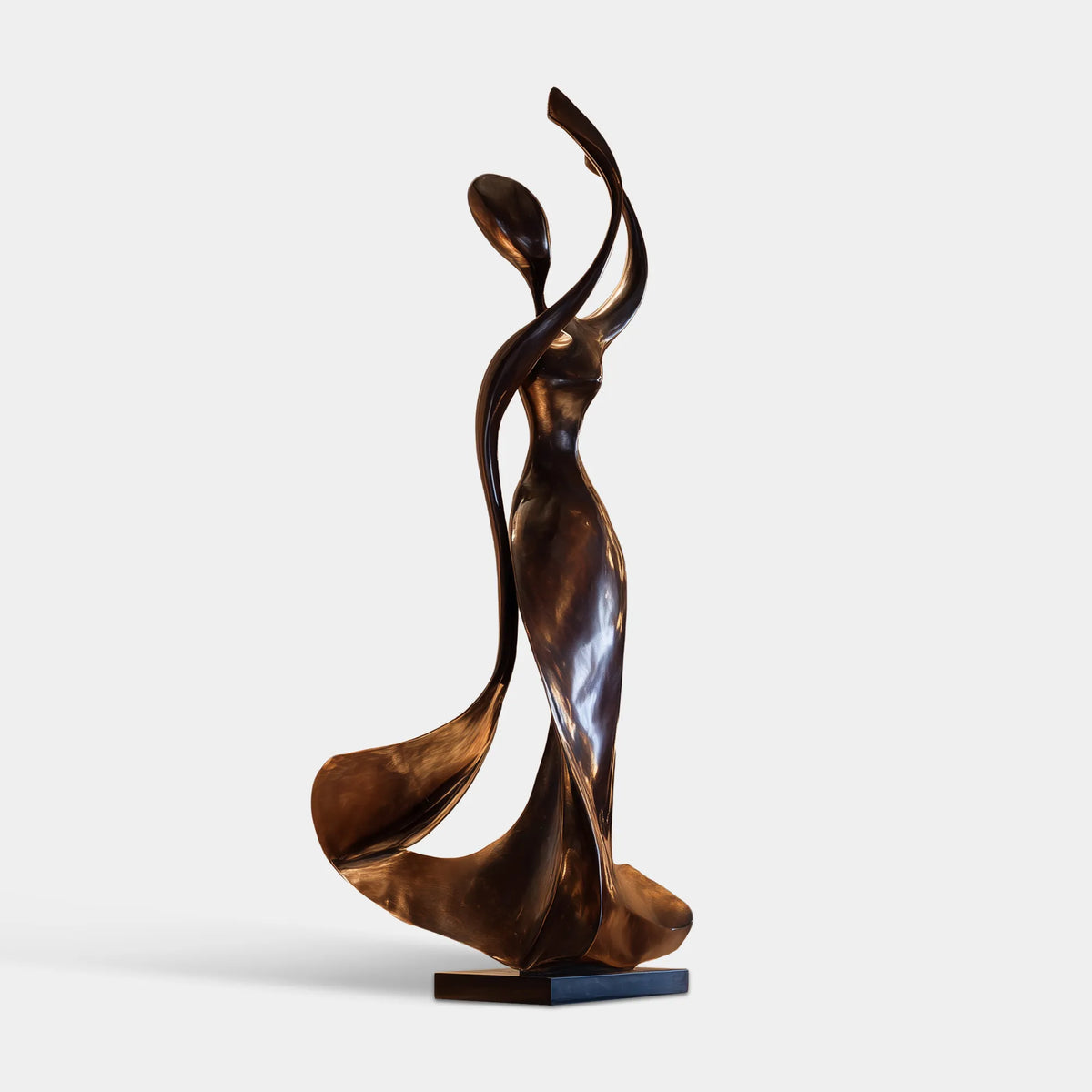 Abstract black stainless steel female sculpture with raised flowing arms and a square black base in a modern home foyer.