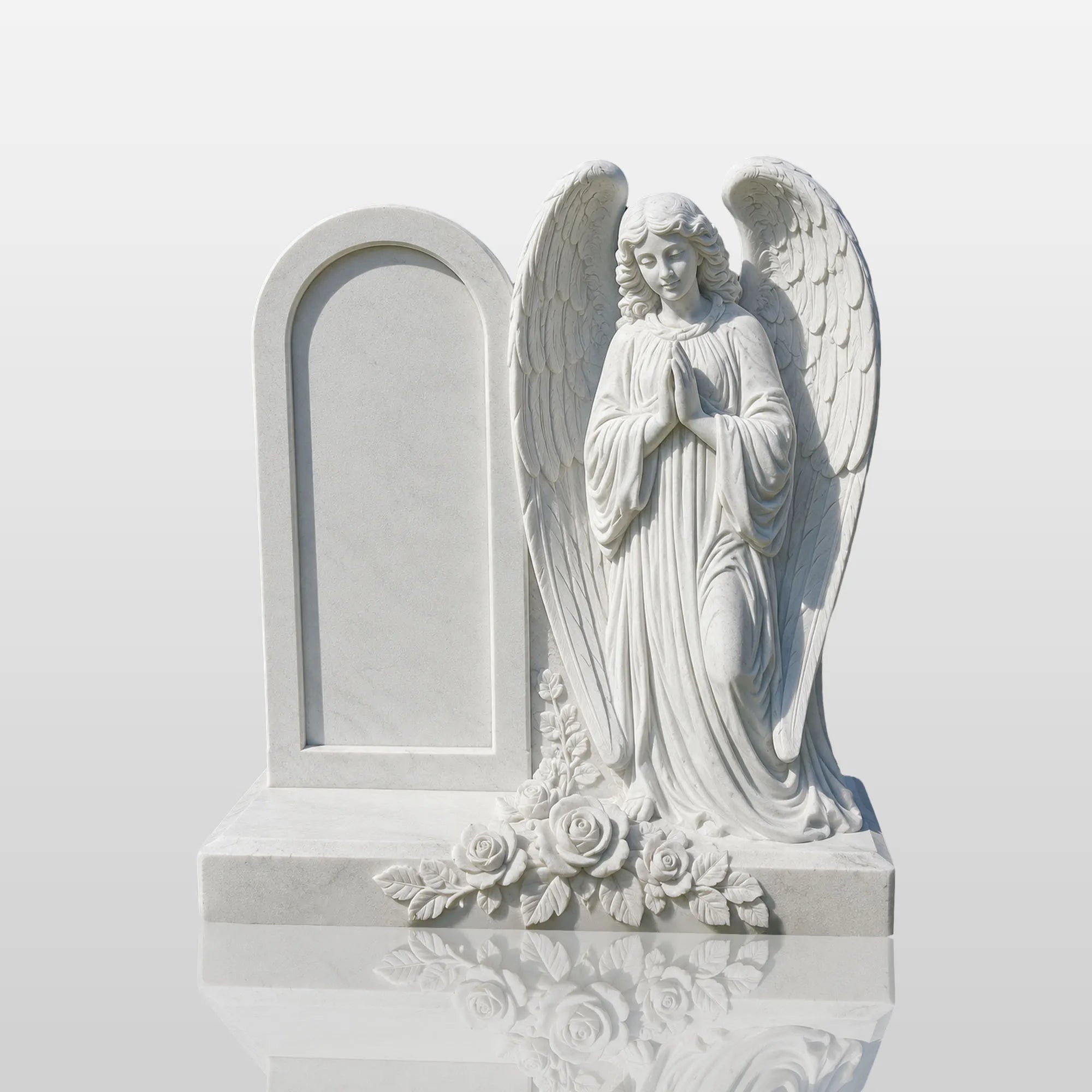 White marble tombstone paired with standing angel statue and carved rose blooms sits on green grass field.