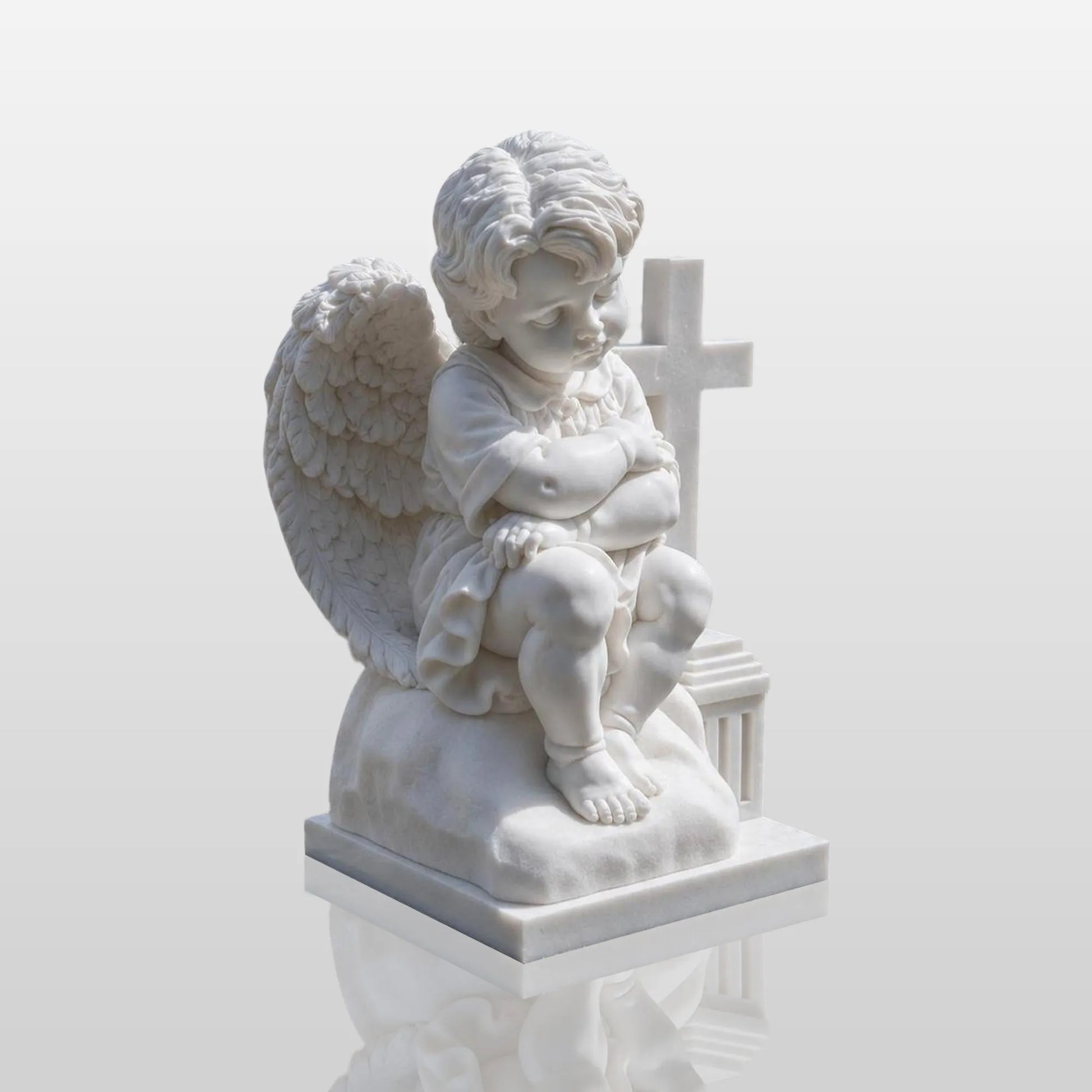 White marble angel child statue sitting beside a cross on a carved stone base for cemetery memorial and family grave.
